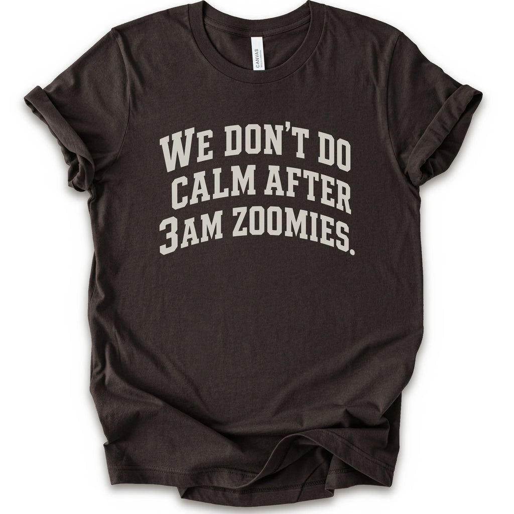 A brown short-sleeve crewneck t-shirt with the text 'WE DON'T DO CALM AFTER 3AM ZOOMIES.' printed in a distressed white font on the front.
