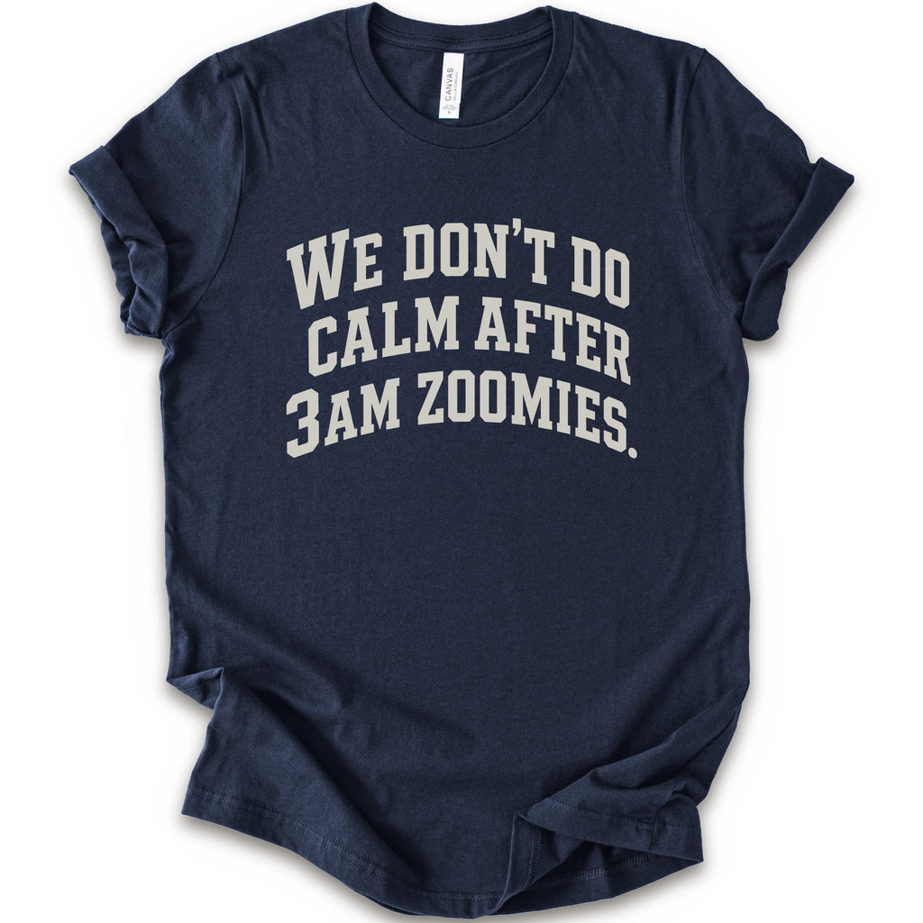 A navy short-sleeve crewneck t-shirt with the text 'WE DON'T DO CALM AFTER 3AM ZOOMIES.' printed in a distressed white font on the front.