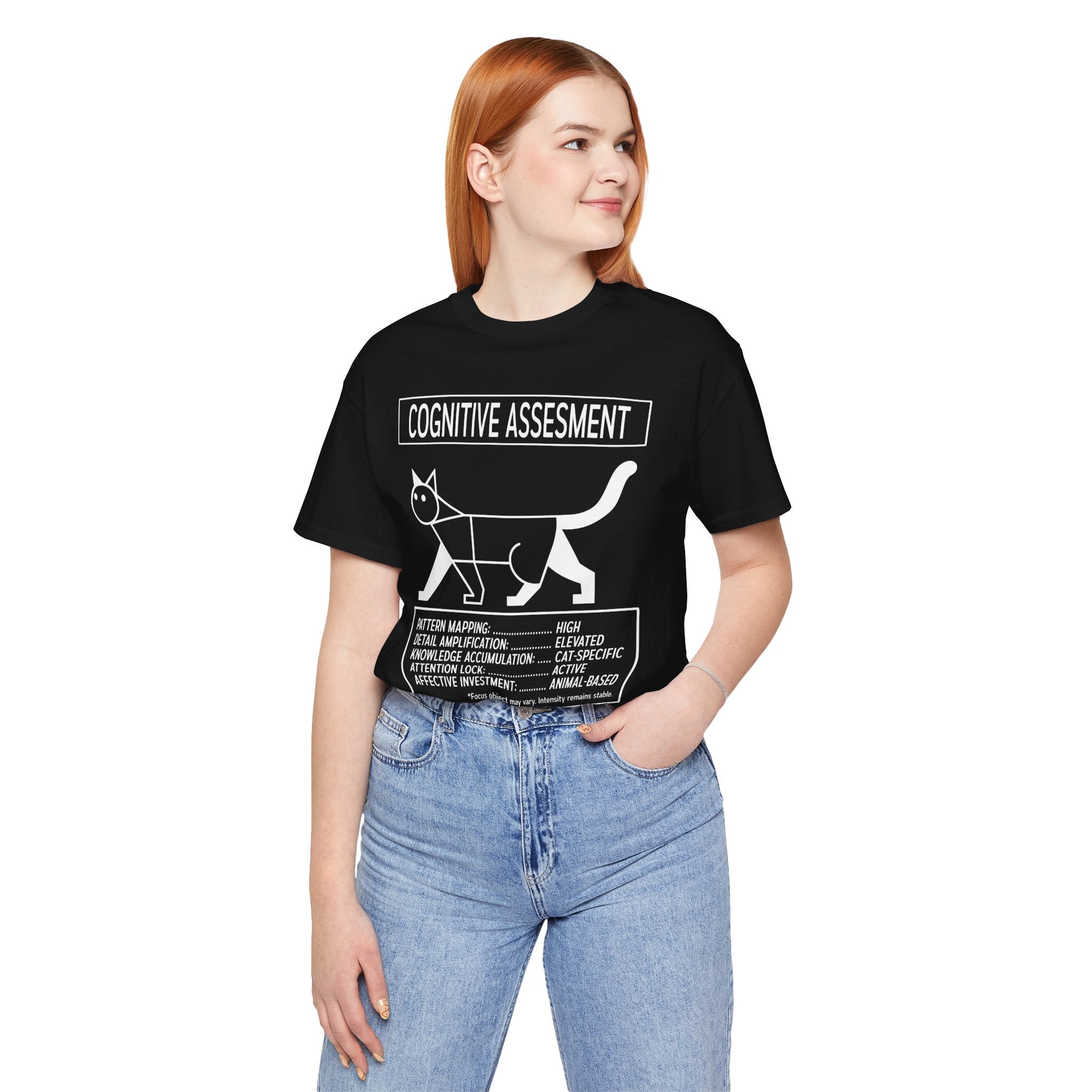 A woman with red hair wearing a black graphic t-shirt with a white cat diagram and the text 'COGNITIVE ASSESSMENT', paired with light blue jeans, against a plain white background.