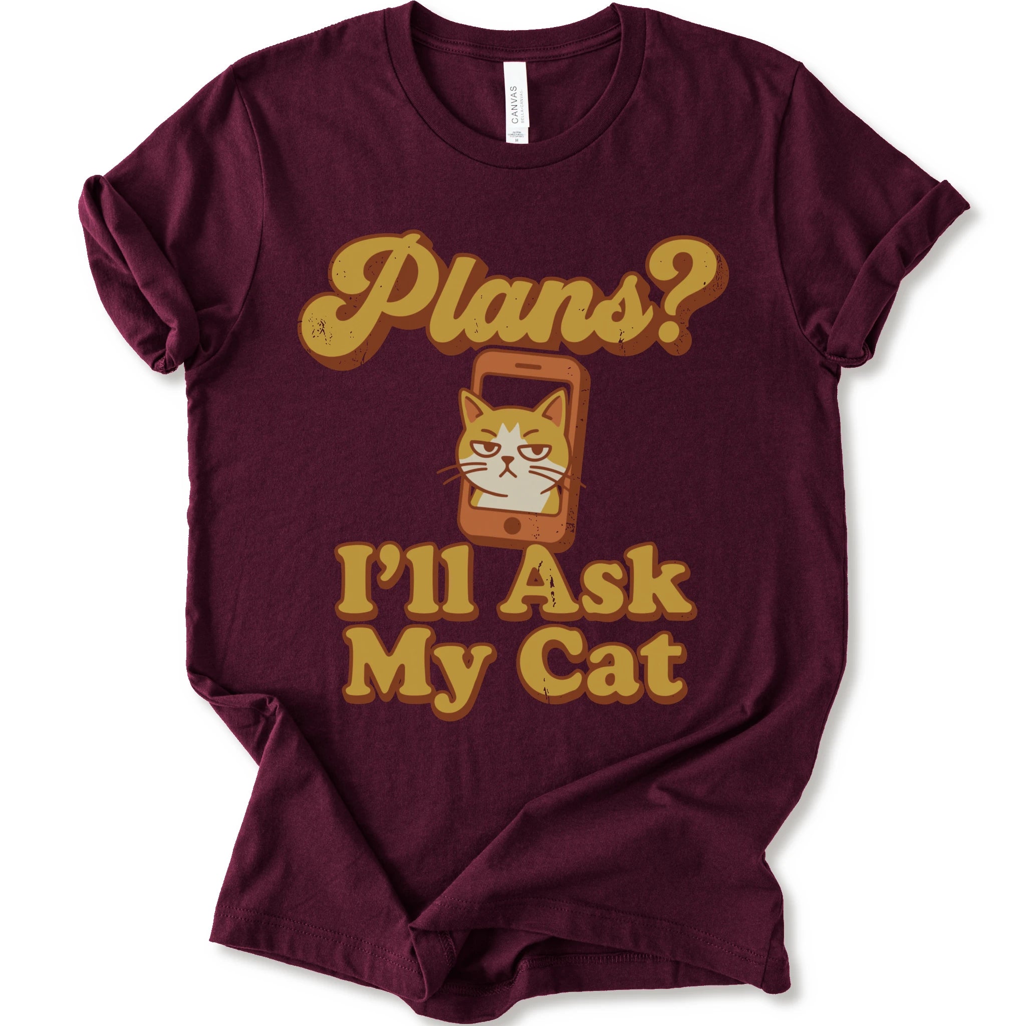 A maroon crewneck t-shirt with a graphic print that reads 'Plans? I'll Ask My Cat' in a retro yellow-orange font, featuring a grumpy orange tabby cat cartoon inside a smartphone.