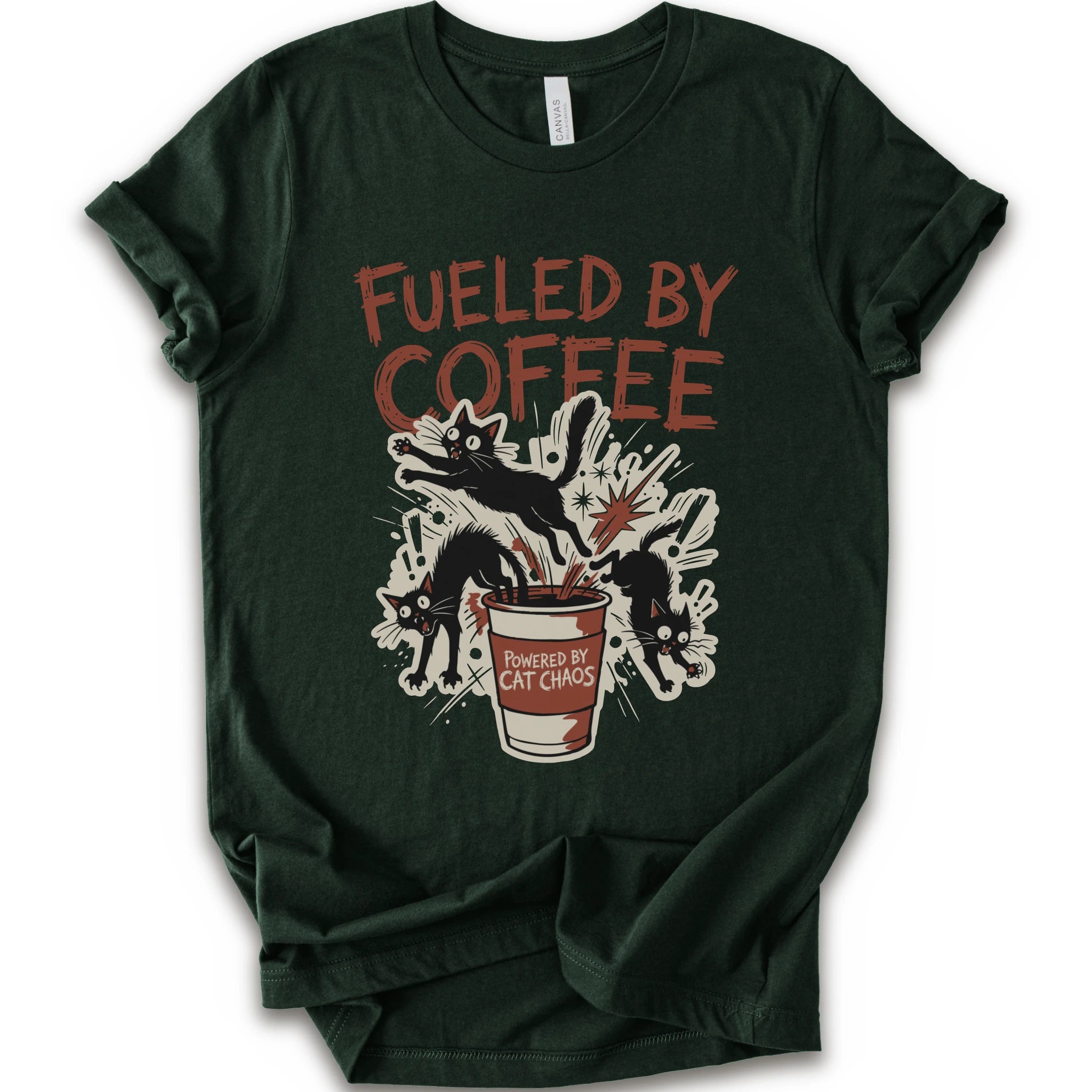 A forest short-sleeve graphic t-shirt laid flat on a white background. The shirt features a distressed graphic print with the text 'FUELED BY COFFEE' in a reddish-brown color, above an illustration of black cats emerging from a coffee cup labeled 'POWERED BY CAT CHAOS'.