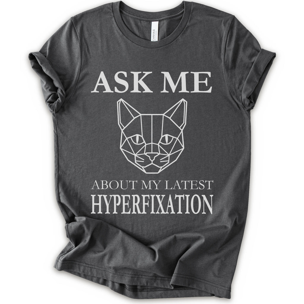 A asphalt short-sleeve t-shirt with a white graphic print featuring a geometric cat face and the text 'ASK ME ABOUT MY LATEST HYPERFIXATION'.