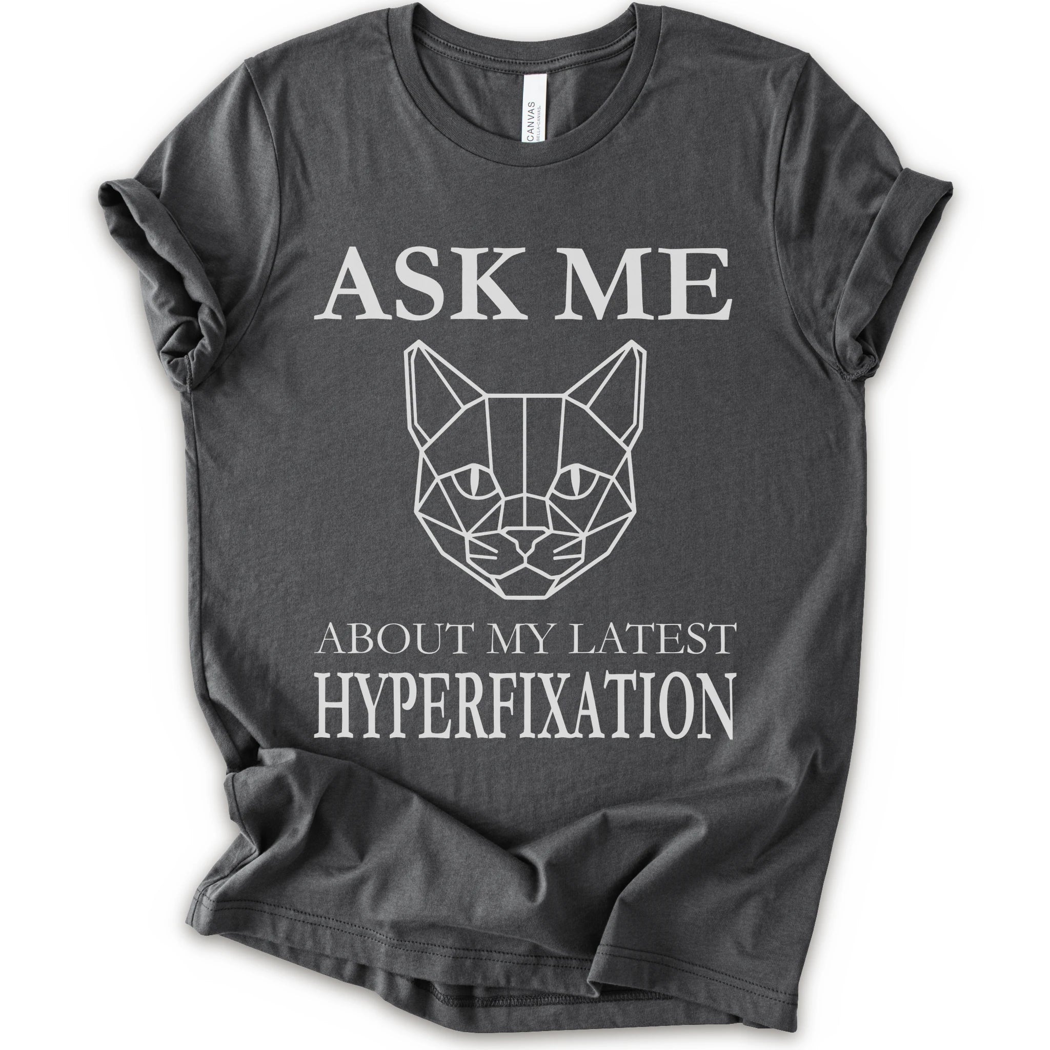 A asphalt short-sleeve t-shirt with a white graphic print featuring a geometric cat face and the text 'ASK ME ABOUT MY LATEST HYPERFIXATION'.