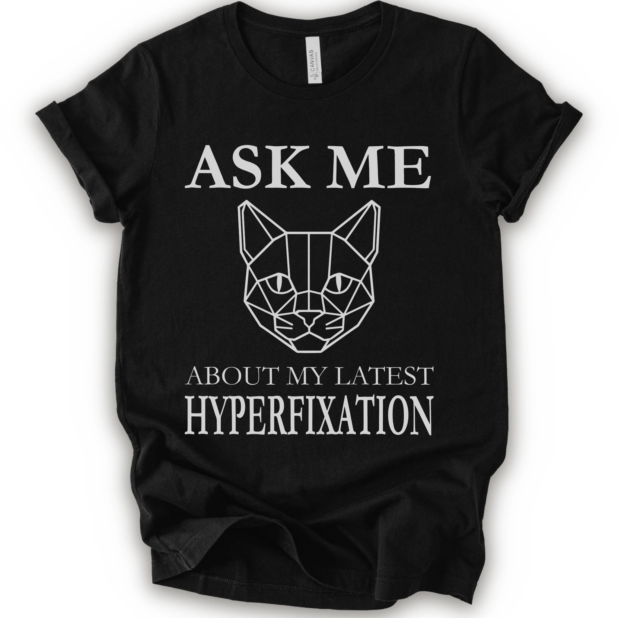 A black short-sleeve t-shirt with a white graphic print featuring a geometric cat face and the text 'ASK ME ABOUT MY LATEST HYPERFIXATION'.