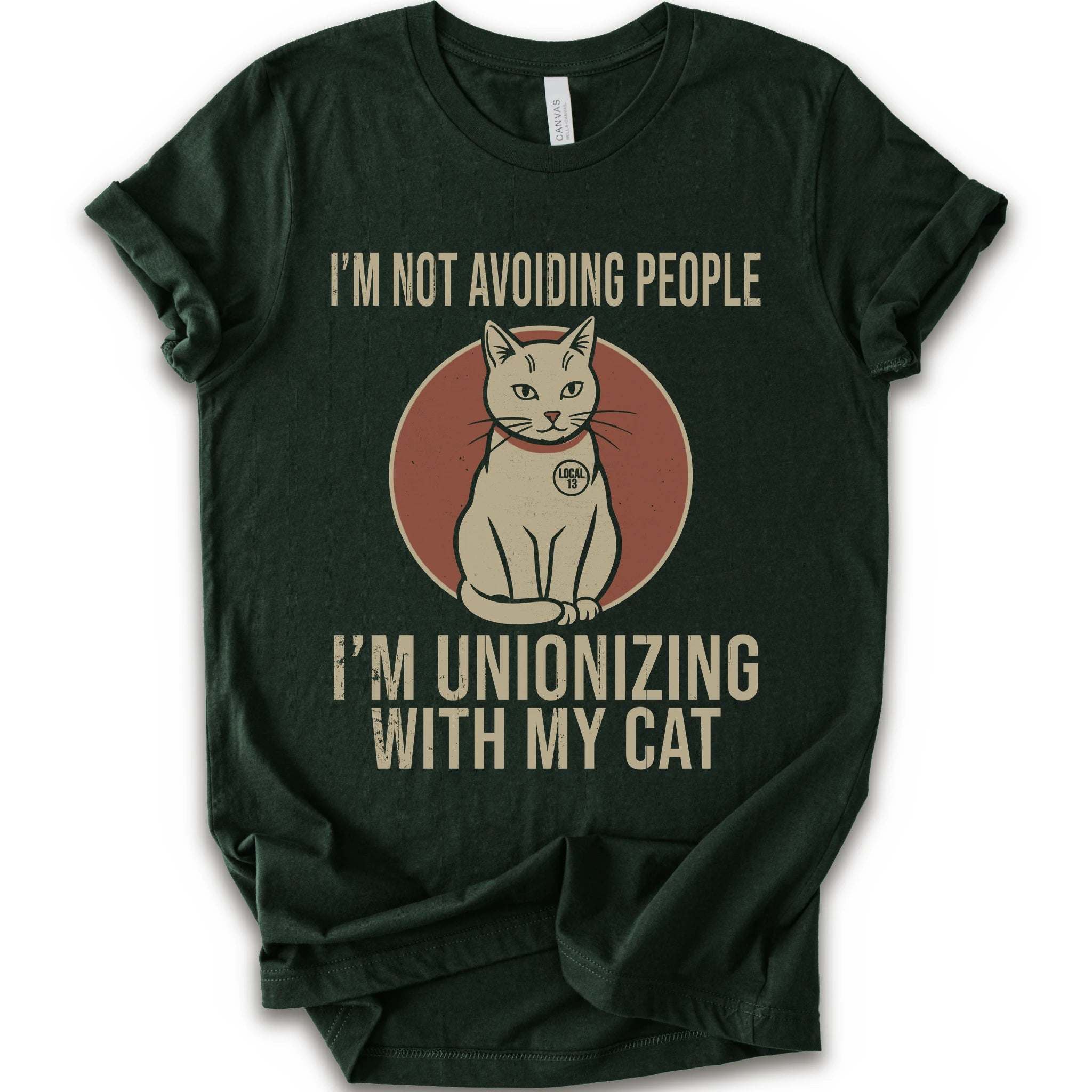 An forest short-sleeve crewneck T-shirt with a retro cat graphic and “I’m Not Avoiding People, I’m Unionizing With My Cat” text.