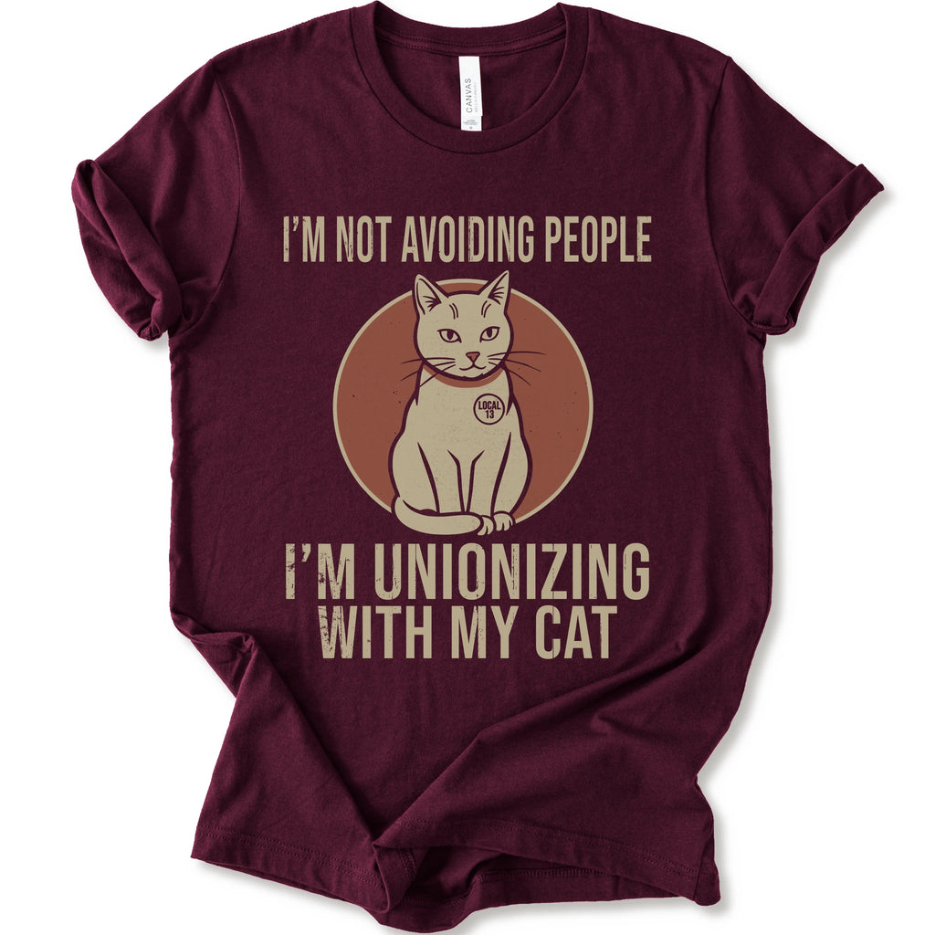 An maroon short-sleeve crewneck T-shirt with a retro cat graphic and “I’m Not Avoiding People, I’m Unionizing With My Cat” text.
