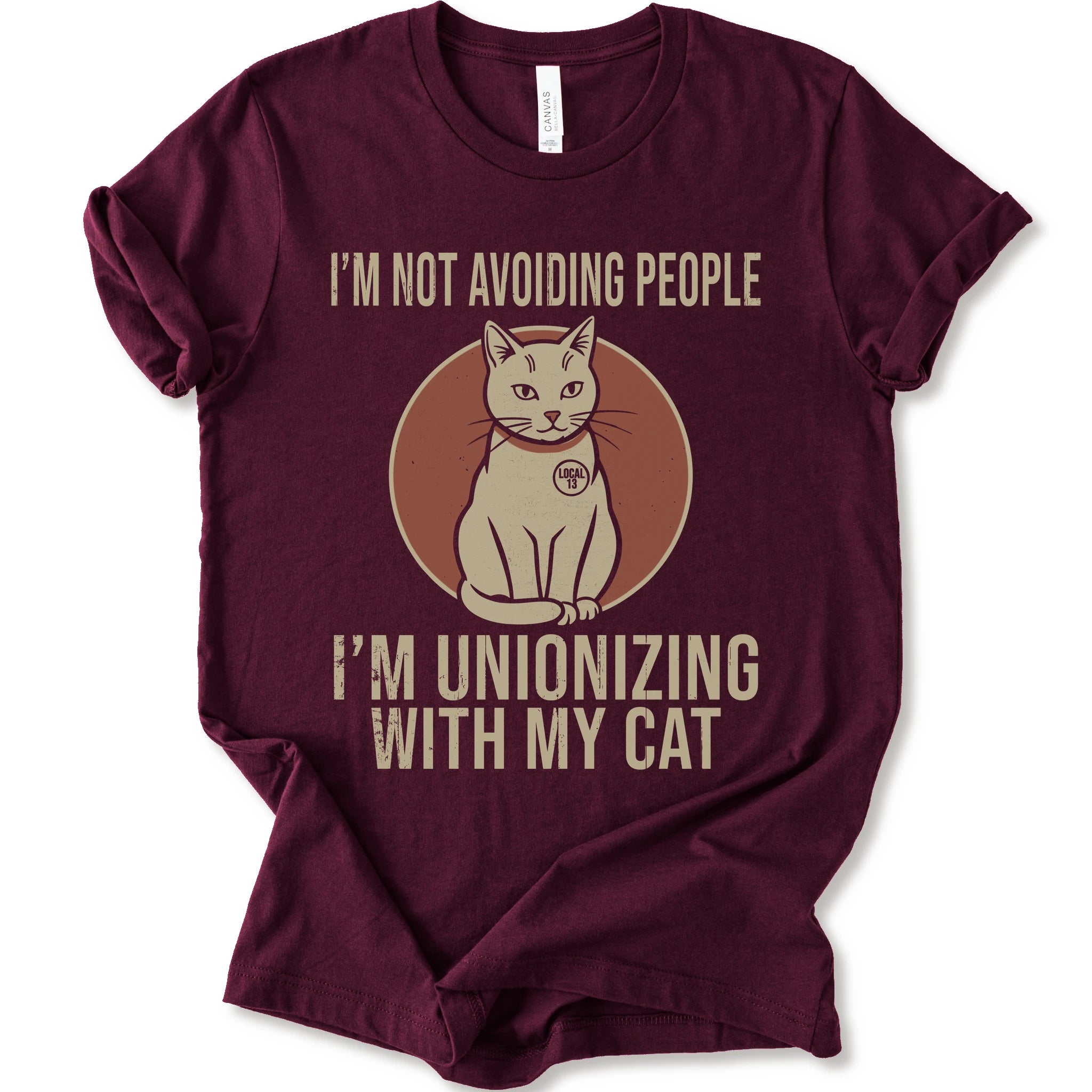 An maroon short-sleeve crewneck T-shirt with a retro cat graphic and “I’m Not Avoiding People, I’m Unionizing With My Cat” text.