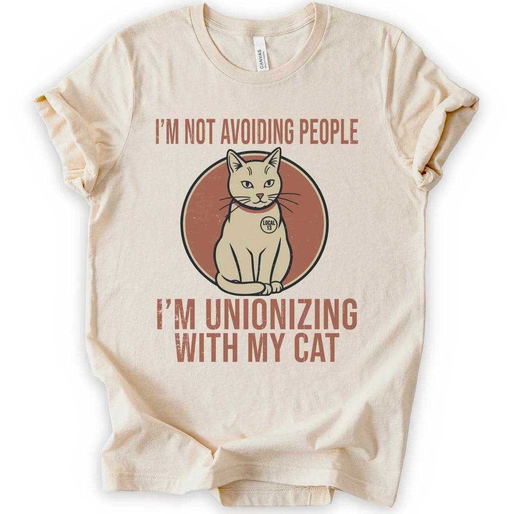 A natural short-sleeve crewneck T-shirt with a retro cat graphic and “I’m Not Avoiding People, I’m Unionizing With My Cat” text.