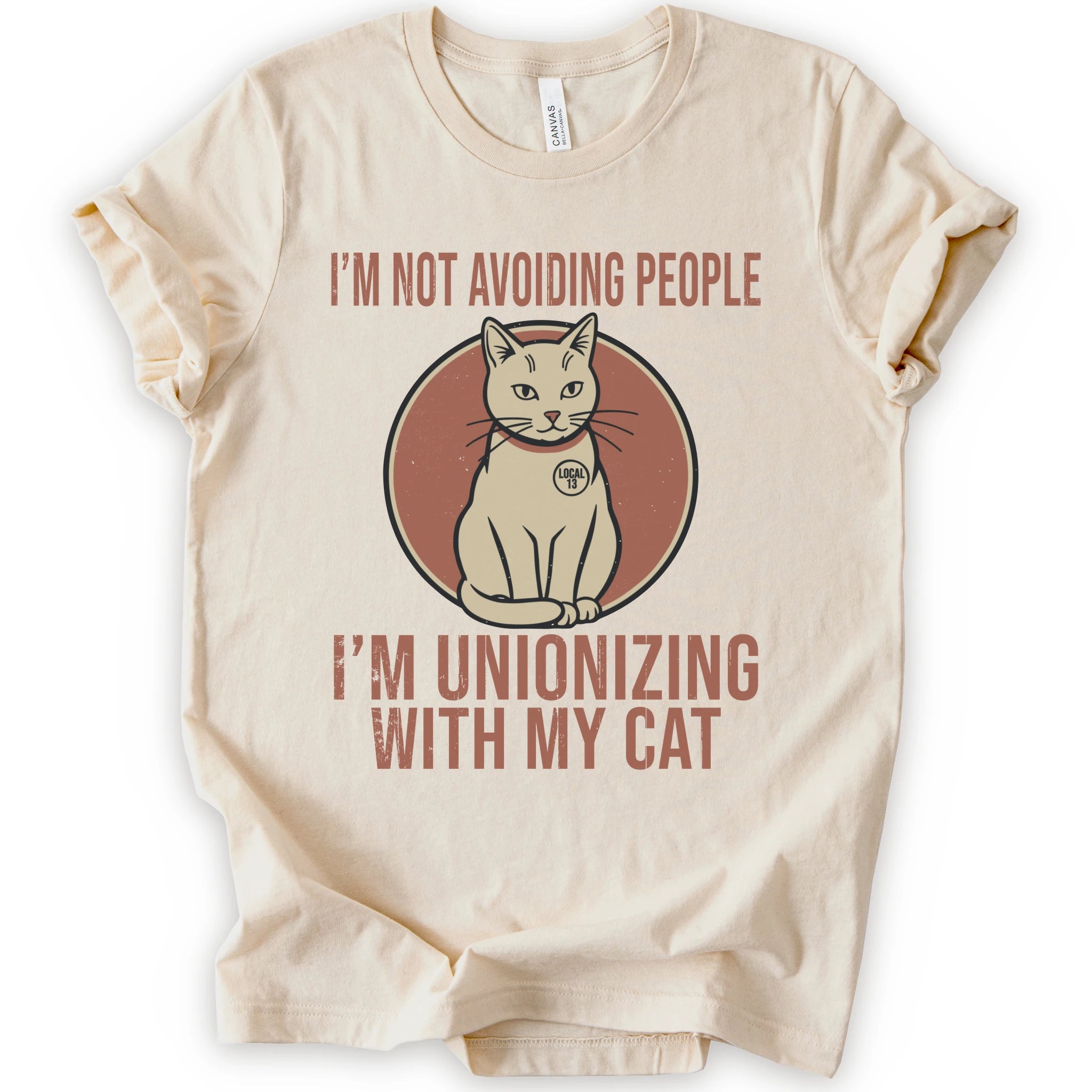 A natural short-sleeve crewneck T-shirt with a retro cat graphic and “I’m Not Avoiding People, I’m Unionizing With My Cat” text.