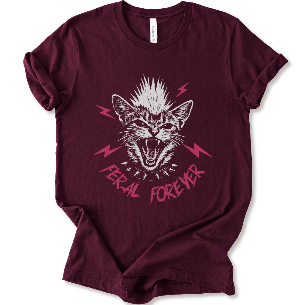 A maroon short-sleeve t-shirt with a graphic of a snarling cat with a mohawk, pink lightning bolts, and the text 'FERAL FOREVER' in pink.