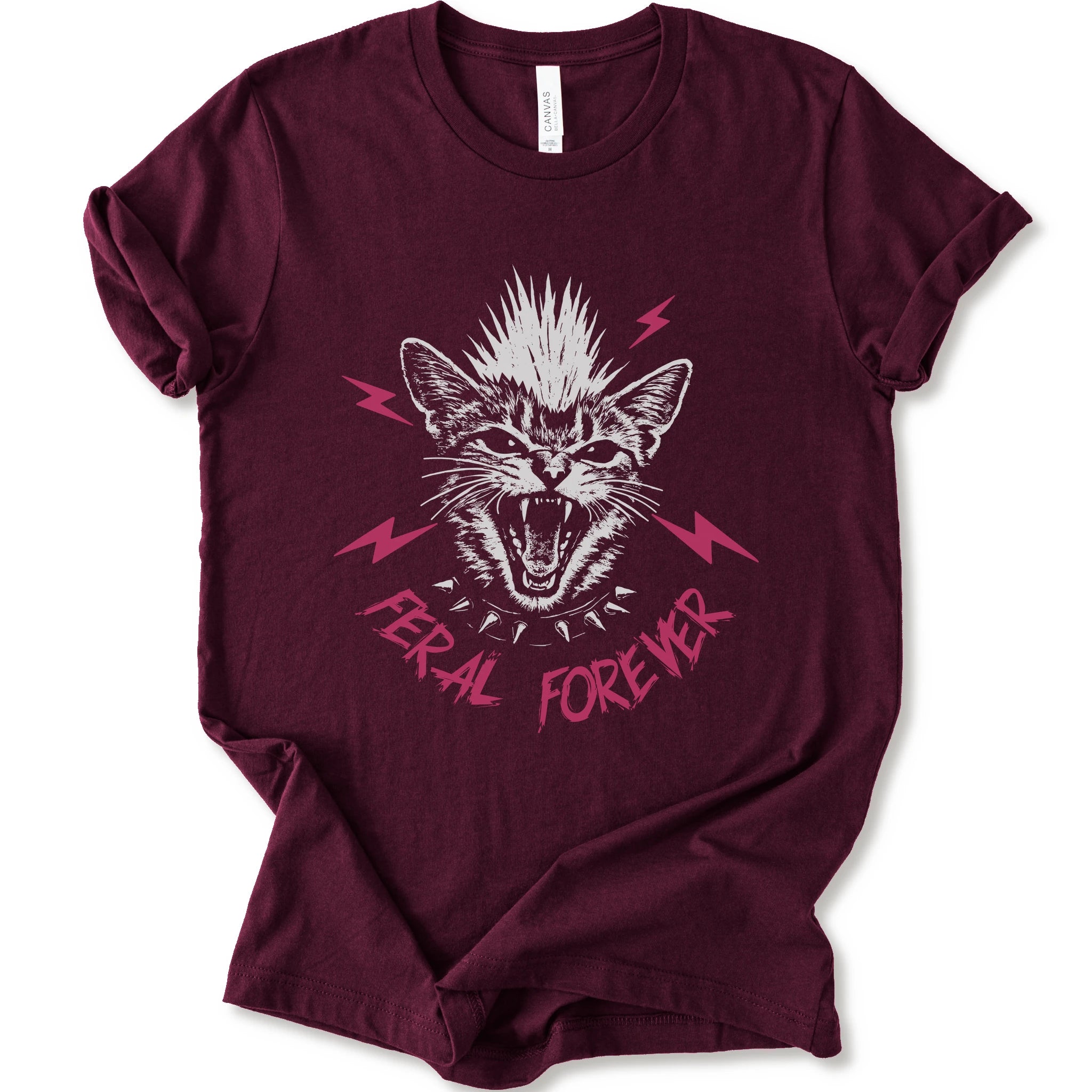 A maroon short-sleeve t-shirt with a graphic of a snarling cat with a mohawk, pink lightning bolts, and the text 'FERAL FOREVER' in pink.