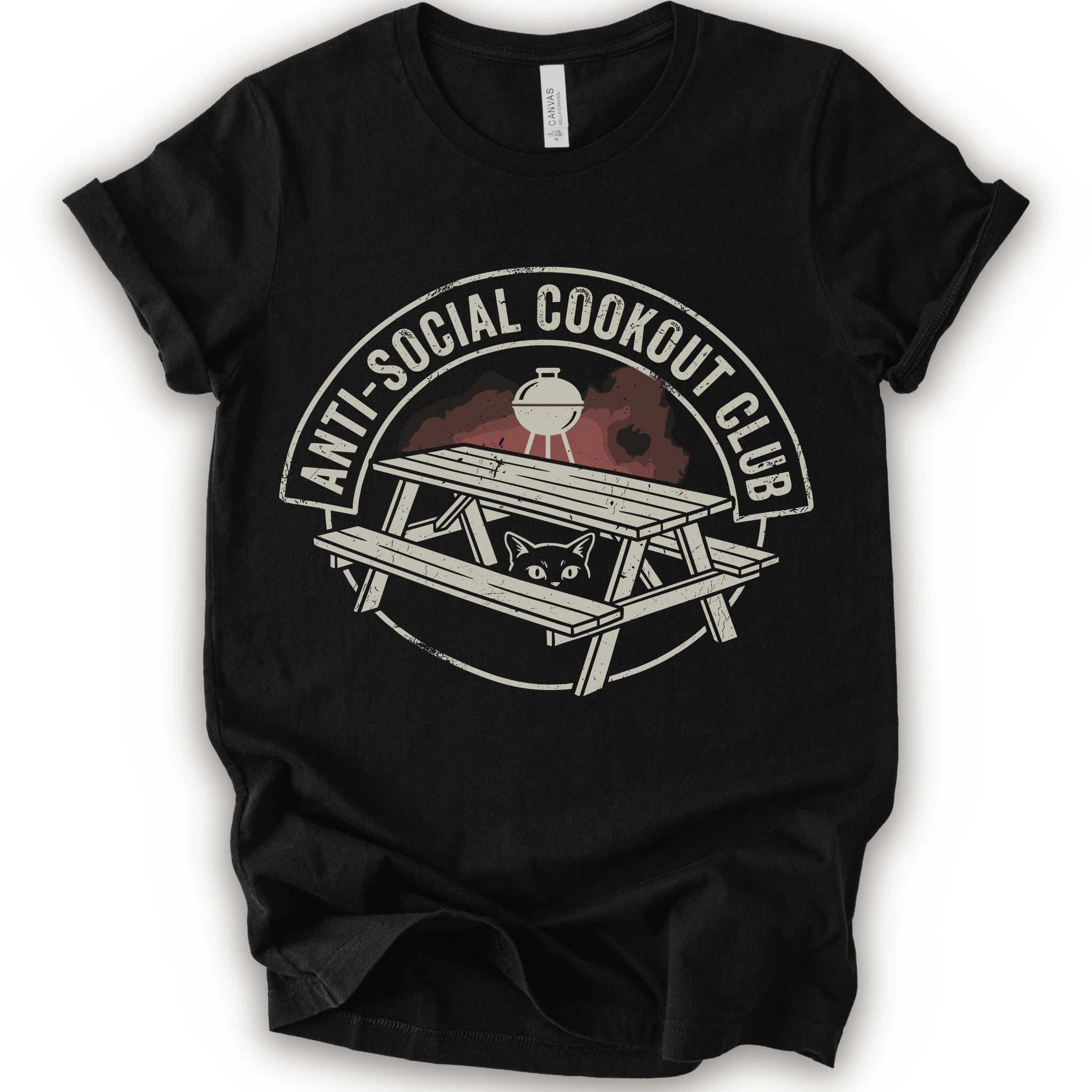 A black short-sleeve crewneck t-shirt with a distressed graphic on the front. The graphic features a picnic table, a grill, and a cat peeking out from underneath, enclosed in a circle with the text 'ANTI-SOCIAL COOKOUT CLUB'.