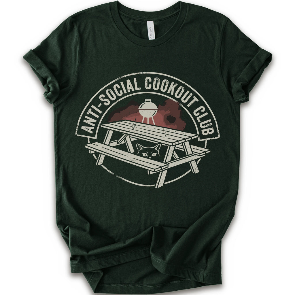 A forest short-sleeve crewneck t-shirt with a distressed graphic on the front. The graphic features a picnic table, a grill, and a cat peeking out from underneath, enclosed in a circle with the text 'ANTI-SOCIAL COOKOUT CLUB'.