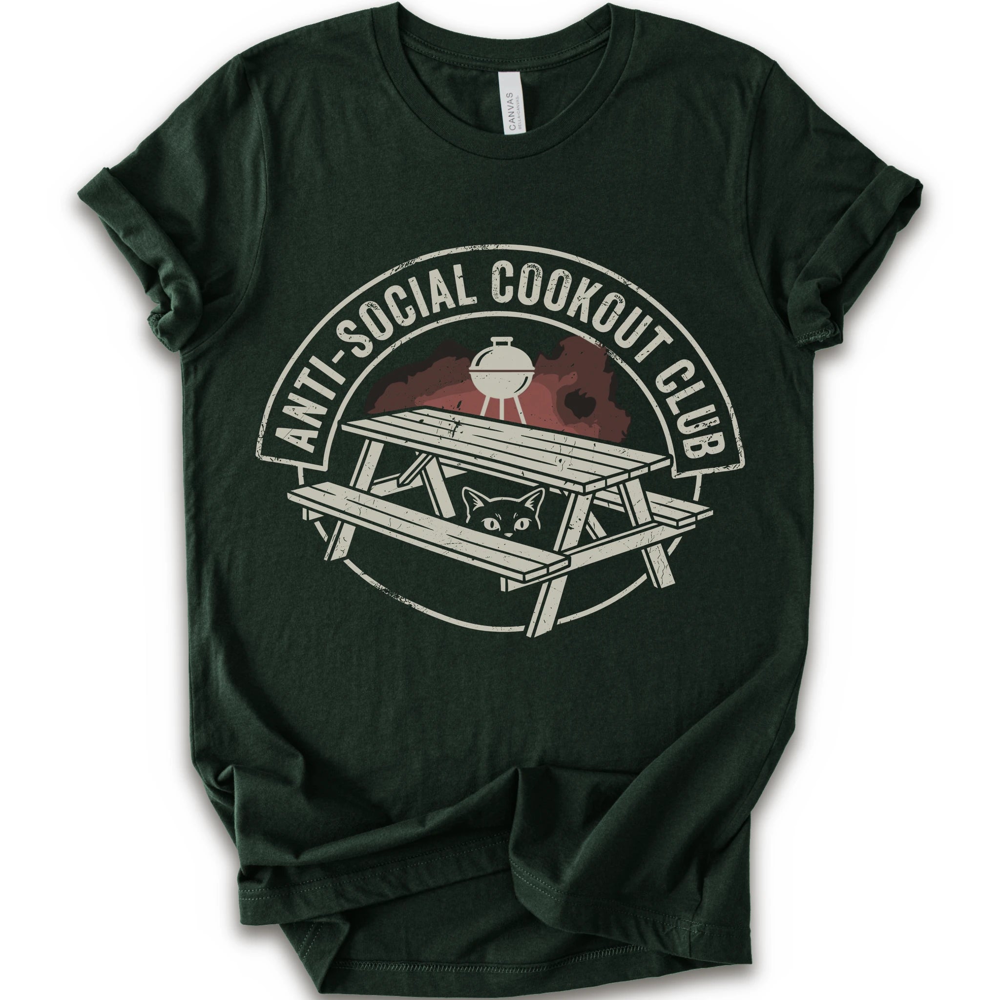 A forest short-sleeve crewneck t-shirt with a distressed graphic on the front. The graphic features a picnic table, a grill, and a cat peeking out from underneath, enclosed in a circle with the text 'ANTI-SOCIAL COOKOUT CLUB'.