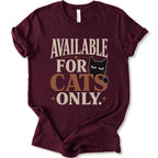 A maroon short-sleeve t-shirt with a distressed graphic that reads 'AVAILABLE FOR CATS ONLY.' in beige and brown-orange lettering, featuring a black cat illustration.