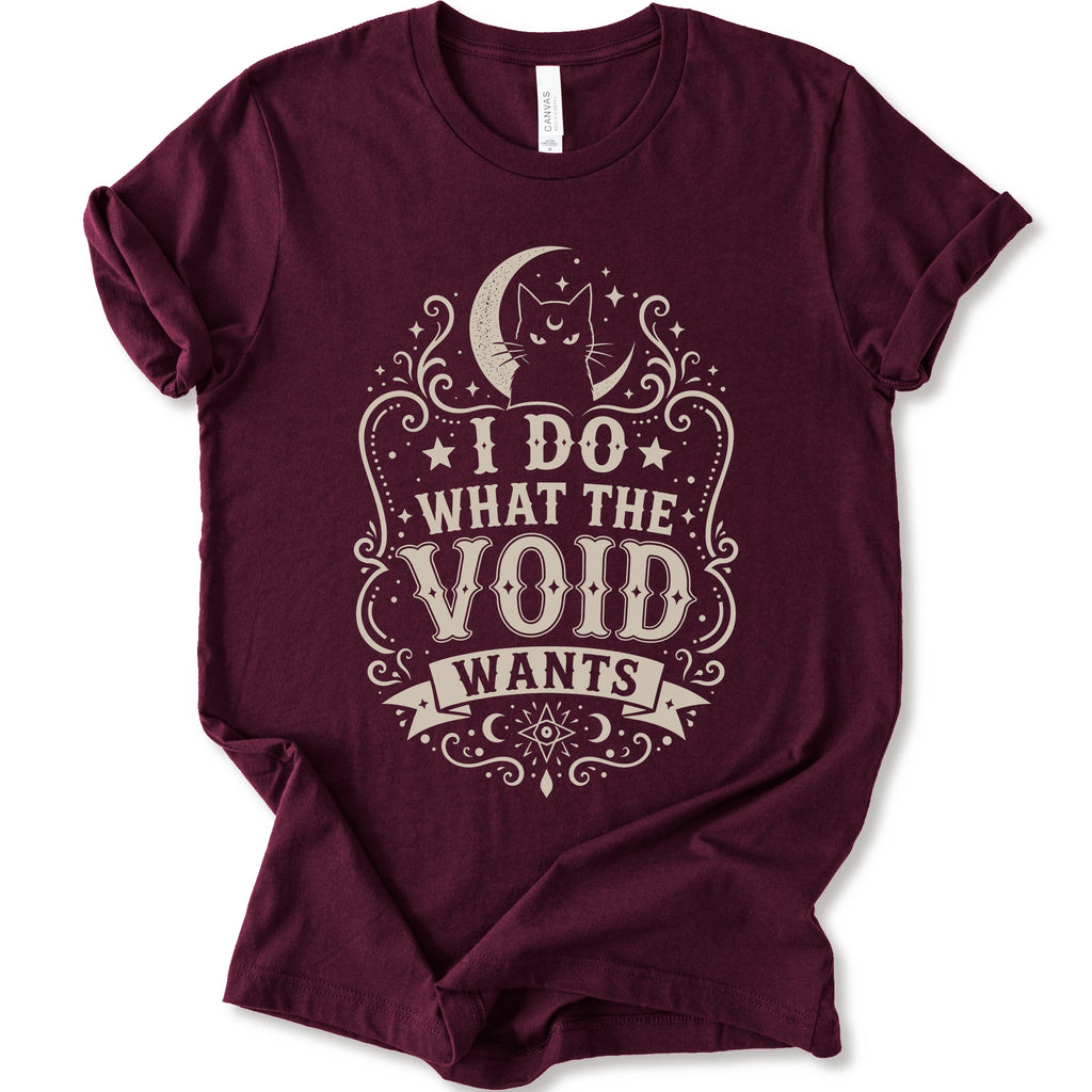Maroon graphic t-shirt with a vintage-style cream graphic on the front. The graphic features a crescent moon, cat silhouette, stars, and the text 'I DO WHAT THE VOID WANTS'.