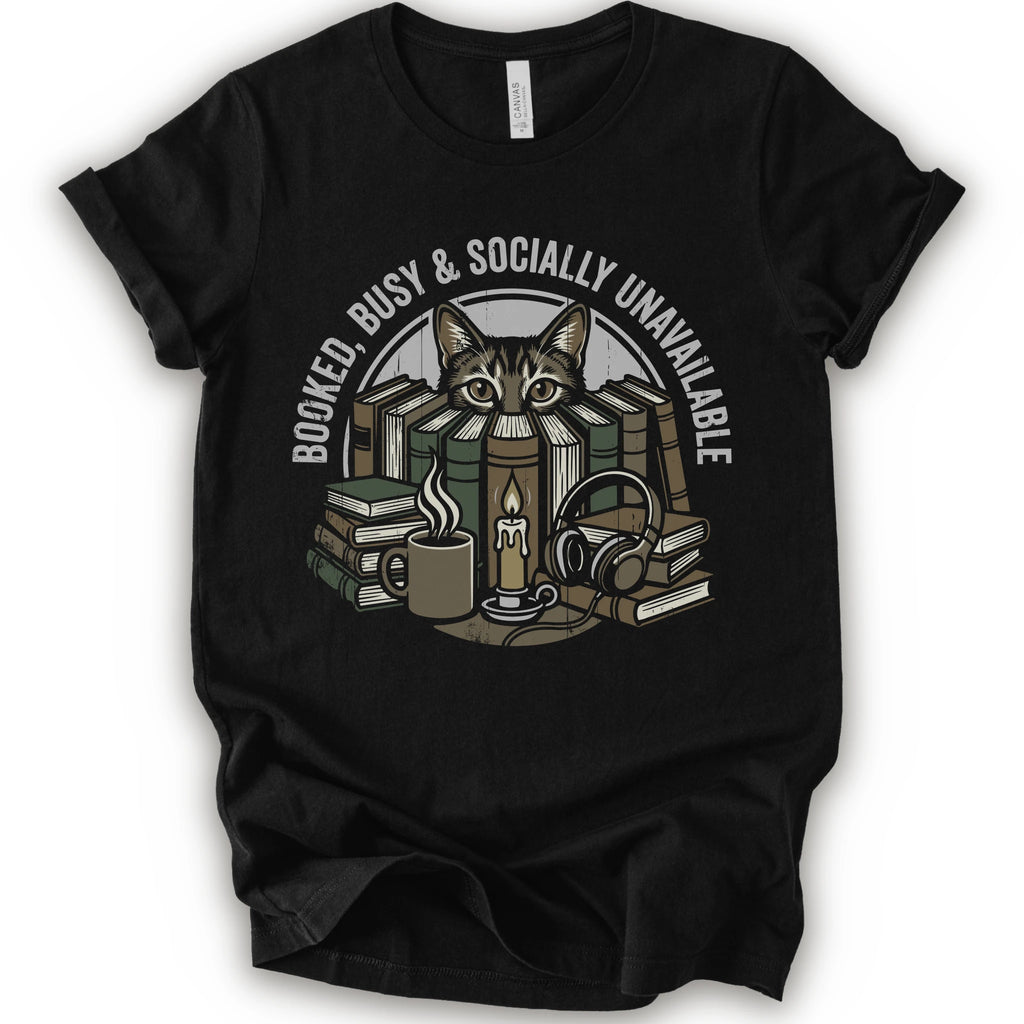 A black short-sleeve crewneck t-shirt with a graphic print of a cat peeking out from stacked books, headphones, and a mug, with the text 'BOOKED BUSY & SOCIALLY UNAVAILABLE' arched above.