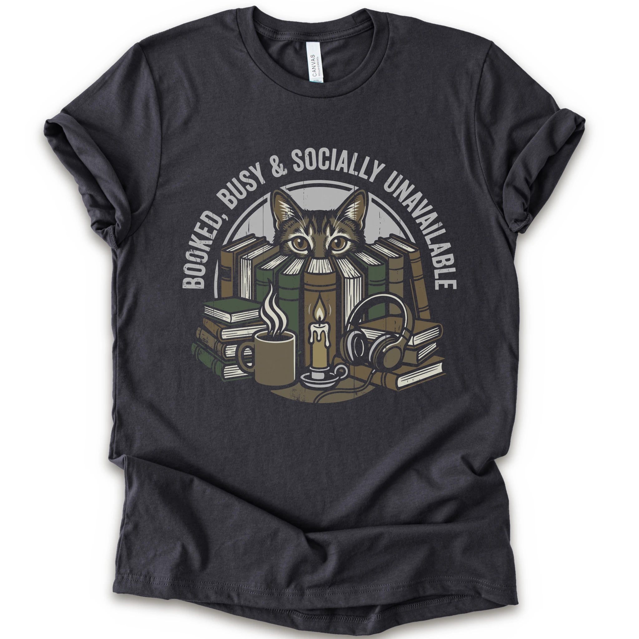 A dark grey short-sleeve crewneck t-shirt with a graphic print of a cat peeking out from stacked books, headphones, and a mug, with the text 'BOOKED BUSY & SOCIALLY UNAVAILABLE' arched above.