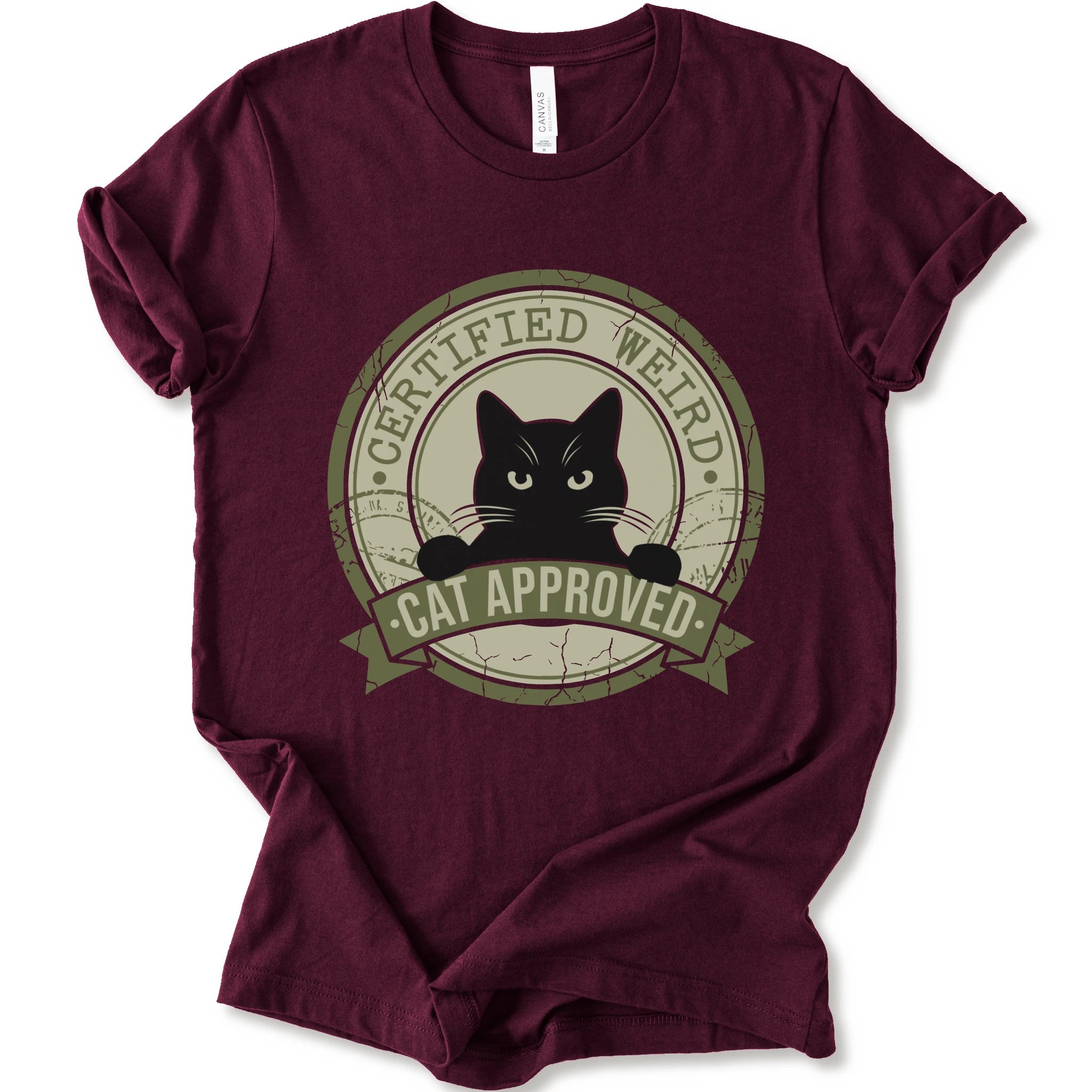 A maroon short-sleeve crewneck t-shirt with a vintage-style circular graphic on the front. The graphic features a black cat peeking out from inside a distressed olive green circle with a banner reading 'CERTIFIED WEIRD - CAT APPROVED'.