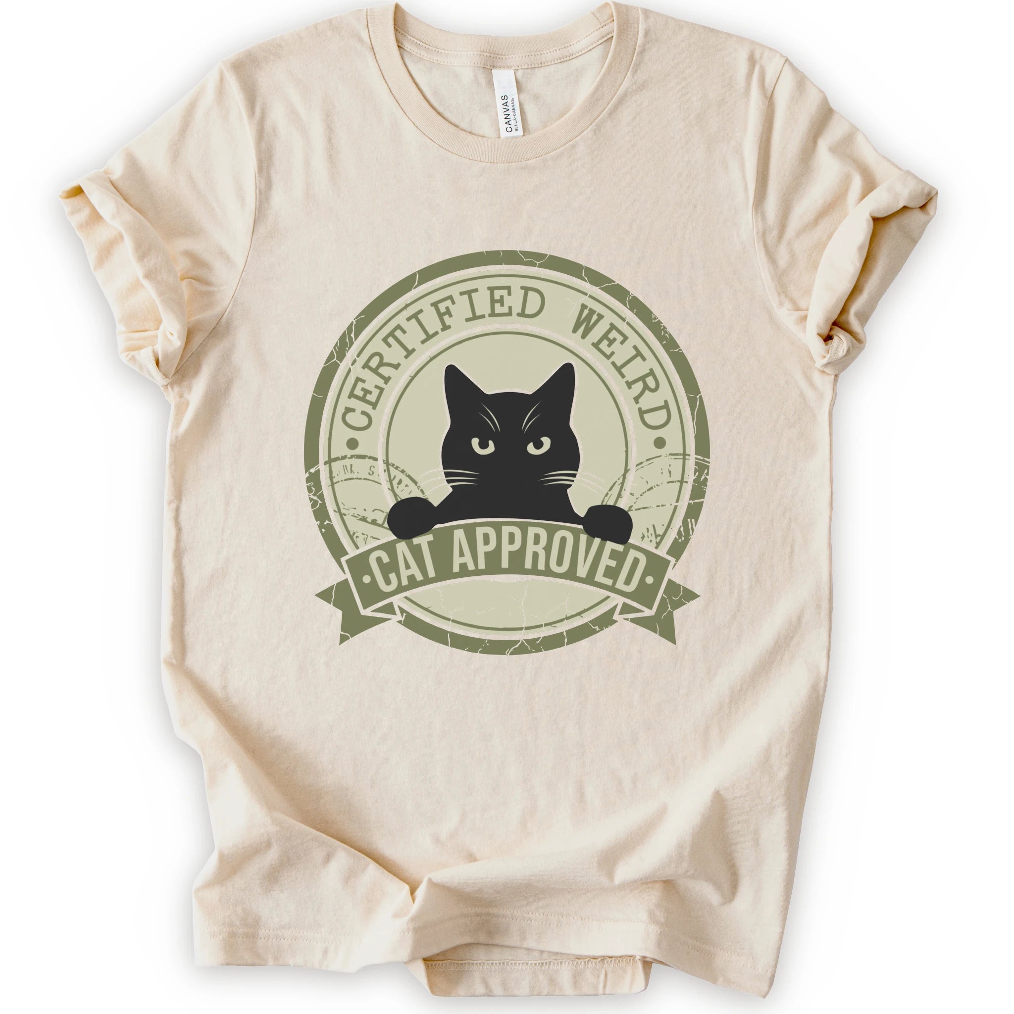 A natural short-sleeve crewneck t-shirt with a vintage-style circular graphic on the front. The graphic features a black cat peeking out from inside a distressed olive green circle with a banner reading 'CERTIFIED WEIRD - CAT APPROVED'.