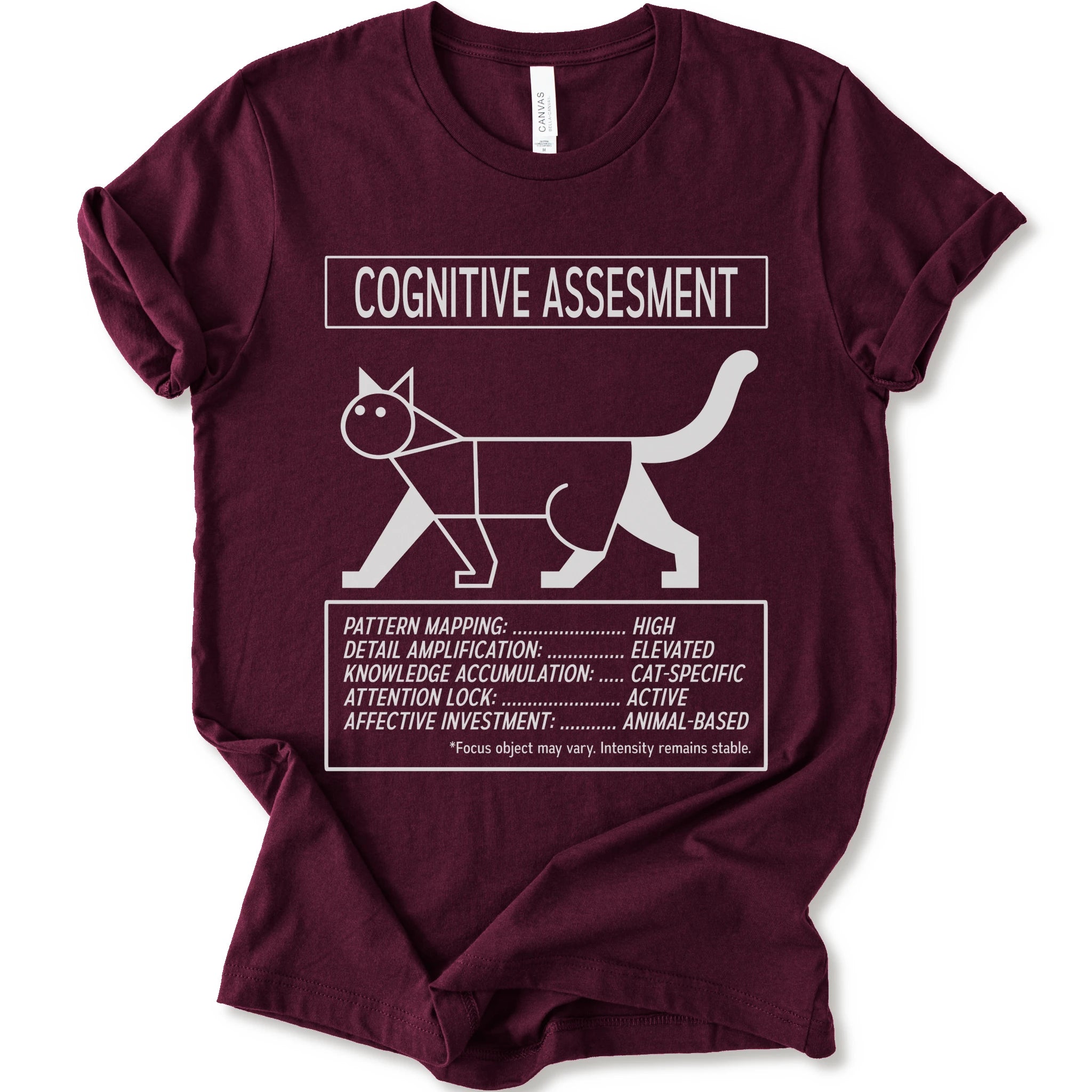 A maroon short-sleeve t-shirt with a white graphic print titled 'COGNITIVE ASSESSMENT' featuring a minimalist line drawing of a cat and a checklist-style design.