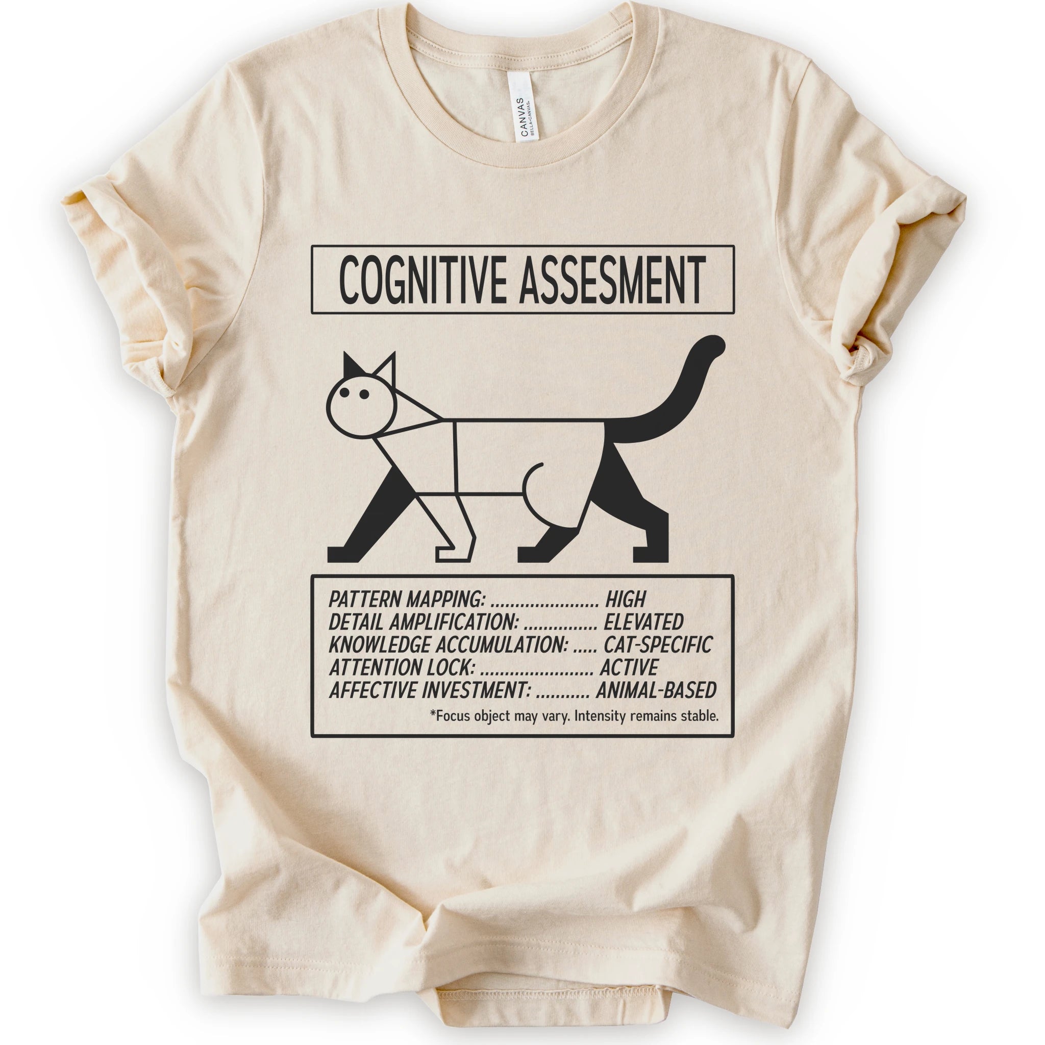 A natural short-sleeve t-shirt with a black graphic print titled 'COGNITIVE ASSESSMENT' featuring a minimalist line drawing of a cat and a checklist-style design.