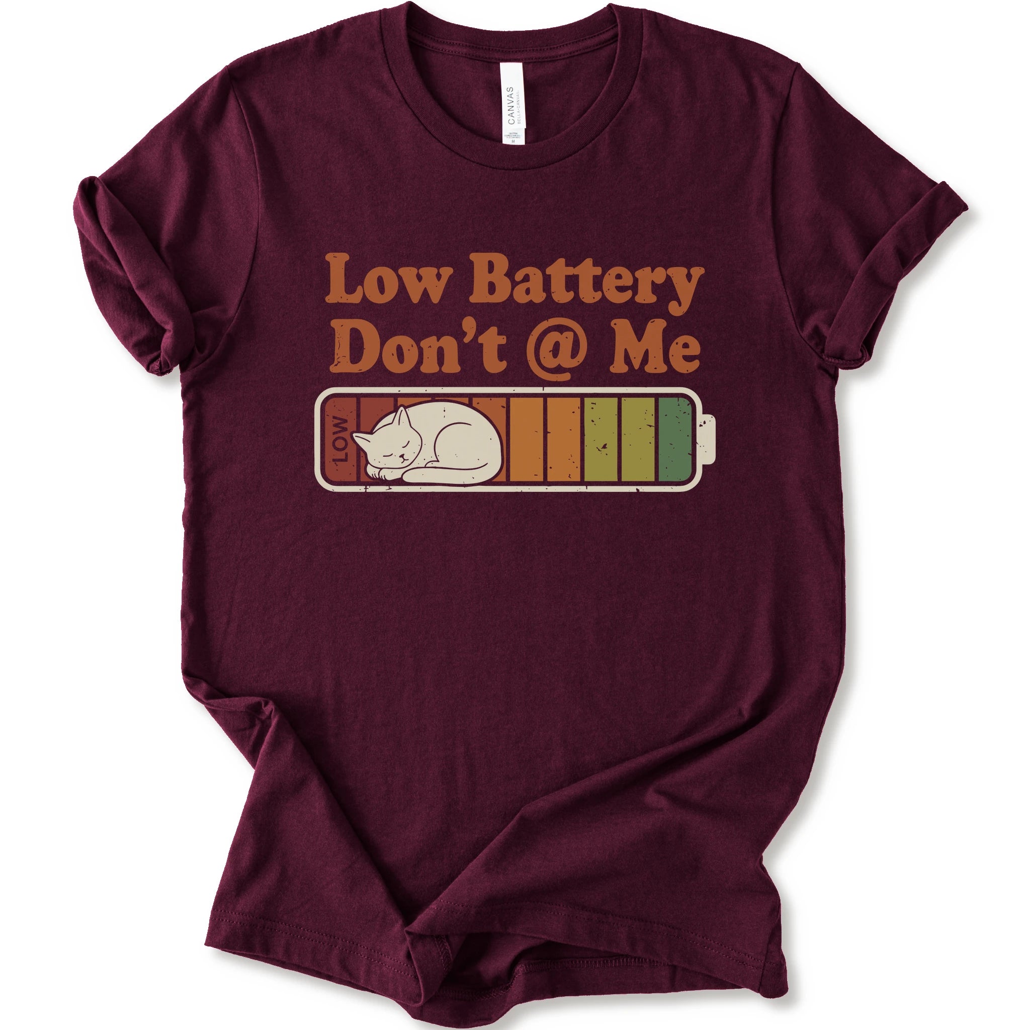 A maroon short-sleeve t-shirt with a graphic print that reads 'Low Battery Don't @ Me' above a retro battery icon containing a sleeping cat.