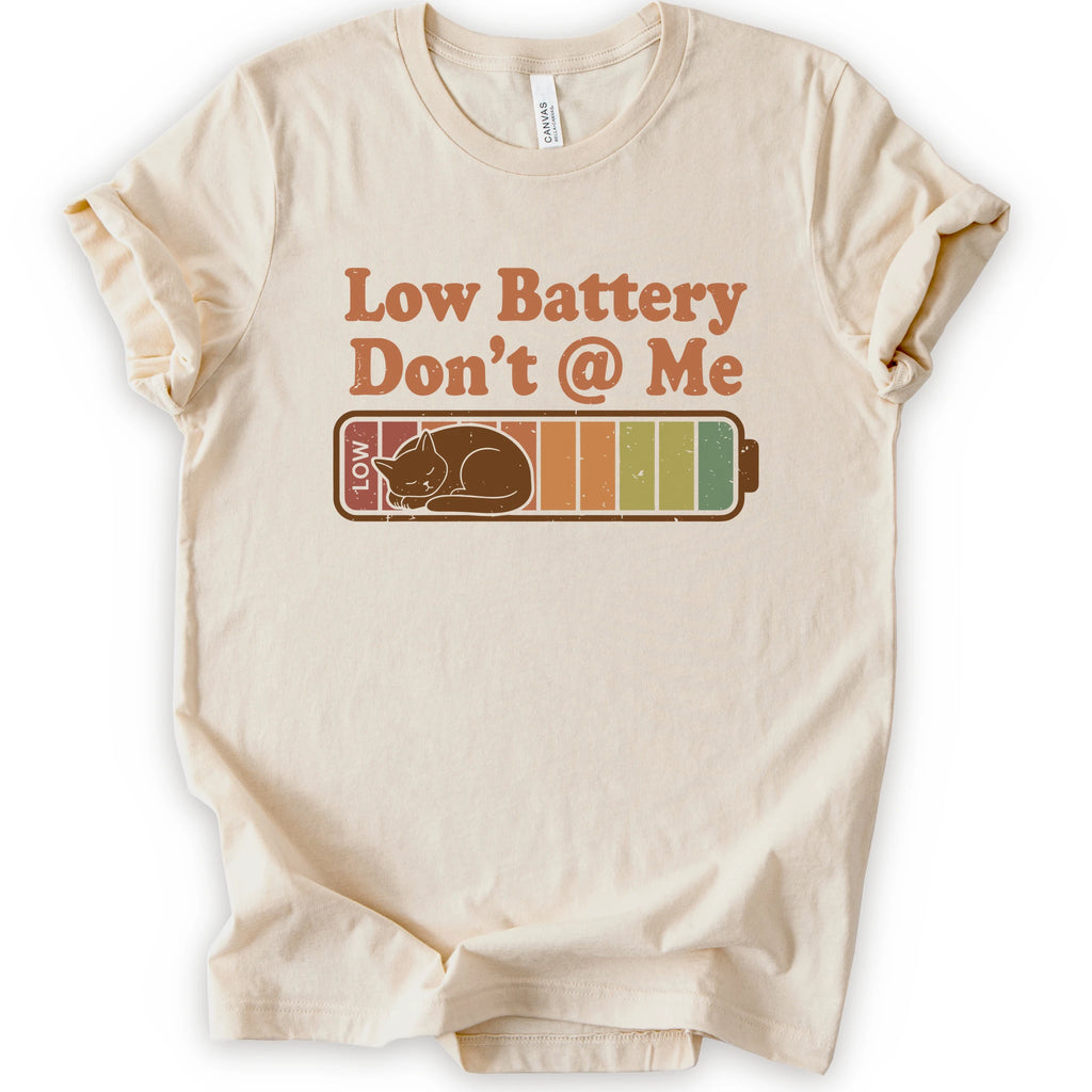 A natural short-sleeve t-shirt with a graphic print that reads 'Low Battery Don't @ Me' above a retro battery icon containing a sleeping cat.