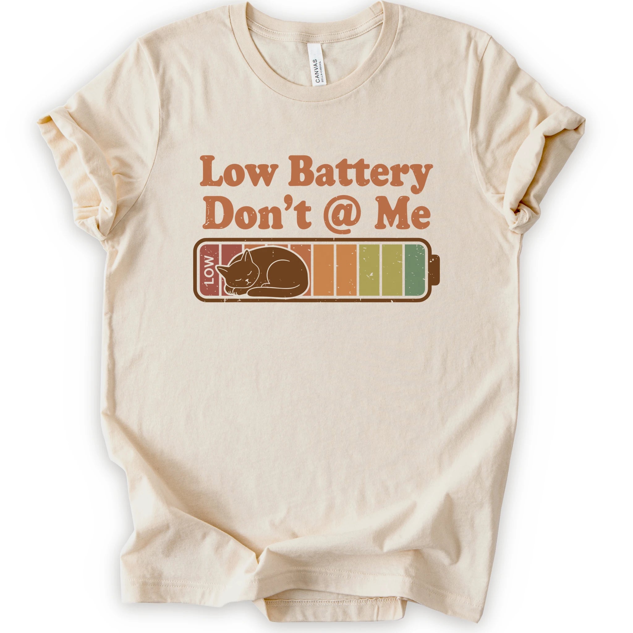 A natural short-sleeve t-shirt with a graphic print that reads 'Low Battery Don't @ Me' above a retro battery icon containing a sleeping cat.
