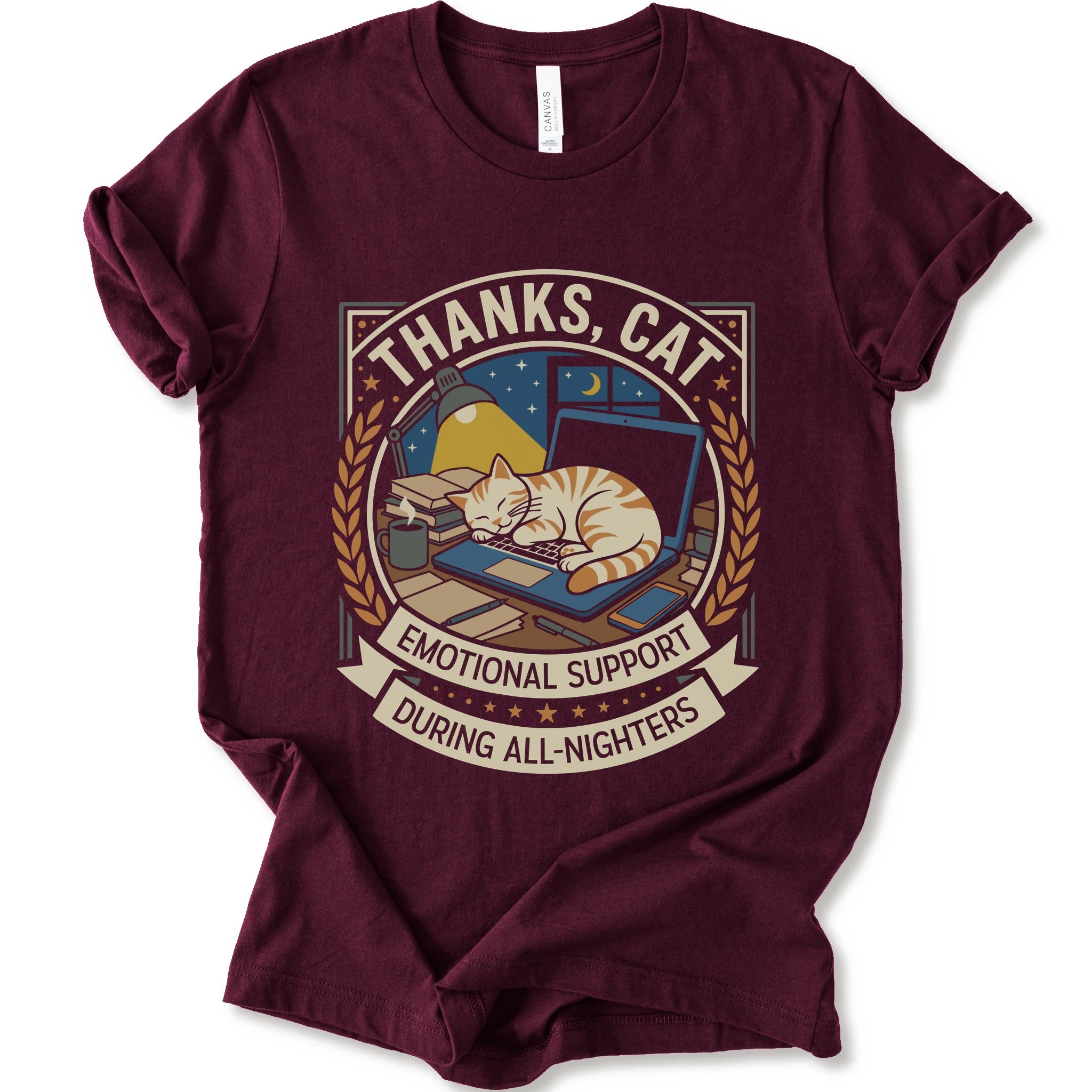 A maroon short-sleeve crewneck t-shirt with a vintage-style graphic on the front. The graphic features an orange tabby cat sleeping on a blue laptop under a night sky, framed by the text 'THANKS, CAT' and 'EMOTIONAL SUPPORT DURING ALL-NIGHTERS'.