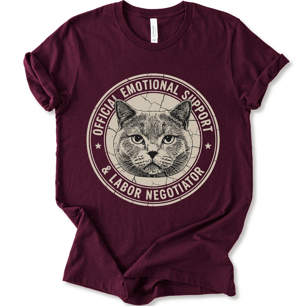 A maroon short-sleeve crewneck t-shirt with a distressed circular graphic on the chest featuring a cat's face and the text 'OFFICIAL EMOTIONAL SUPPORT & LABOR NEGOTIATOR'.