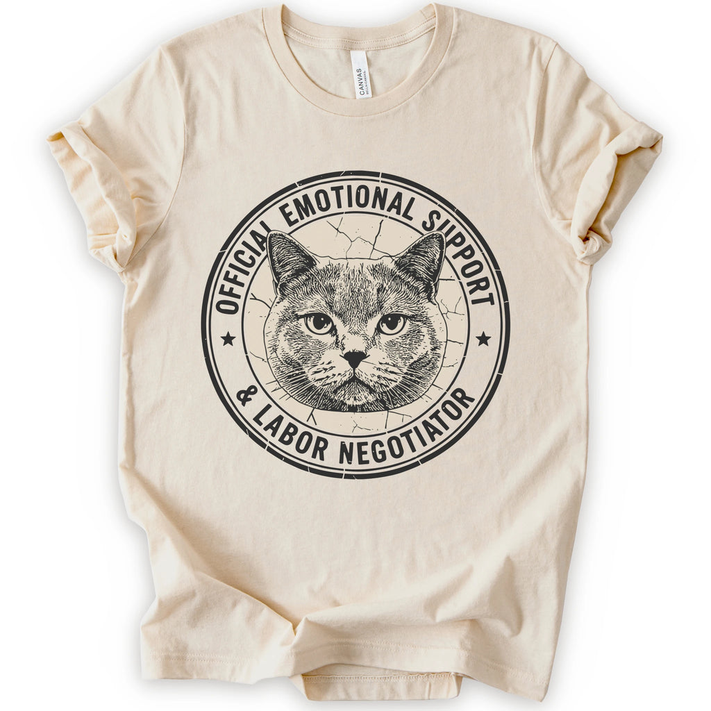 A natural short-sleeve crewneck t-shirt with a distressed circular graphic on the chest featuring a cat's face and the text 'OFFICIAL EMOTIONAL SUPPORT & LABOR NEGOTIATOR'.