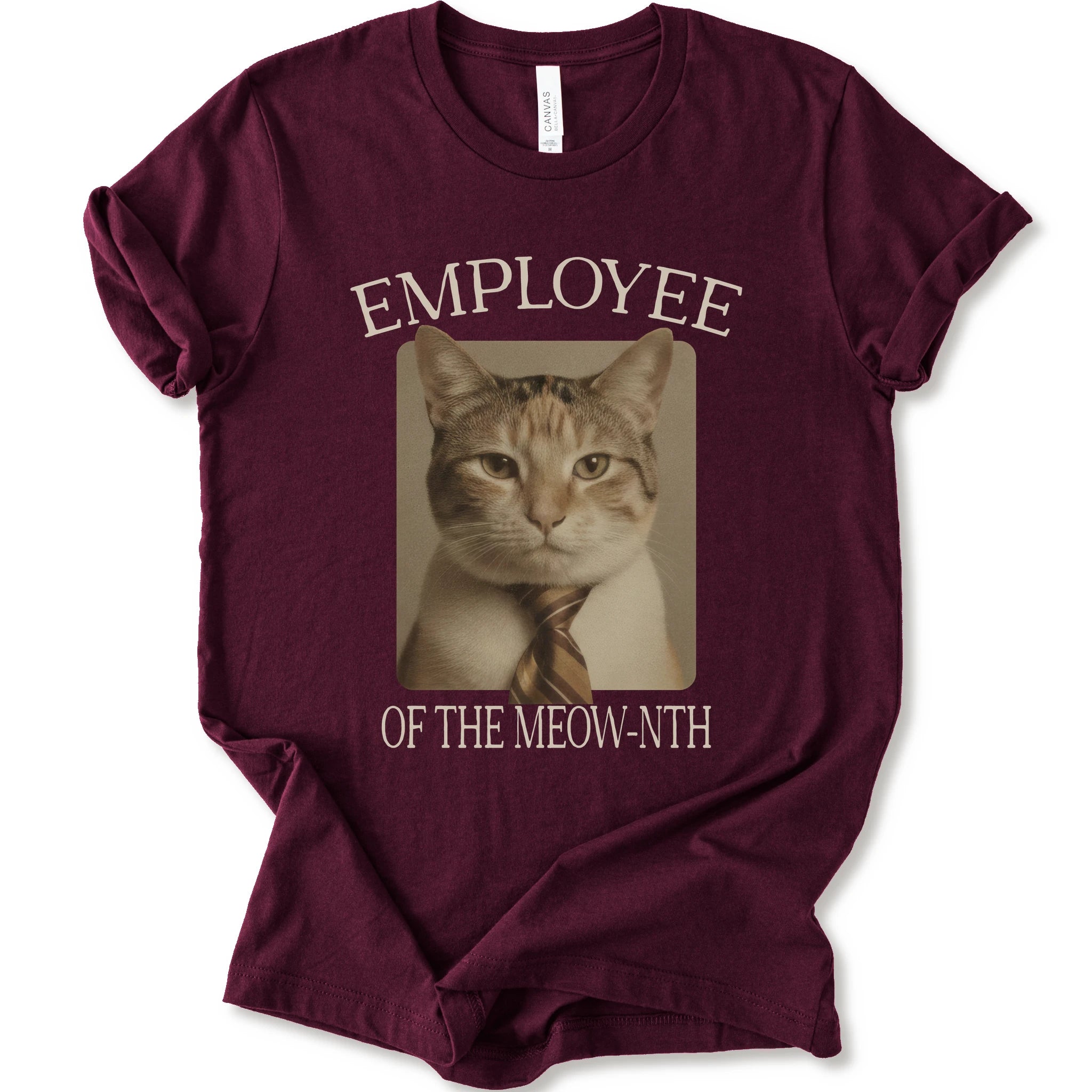 A maroon short-sleeve crewneck t-shirt with a graphic print of a cat wearing a tie inside a beige frame, with the text 'EMPLOYEE OF THE MEOW-NTH' in beige lettering.