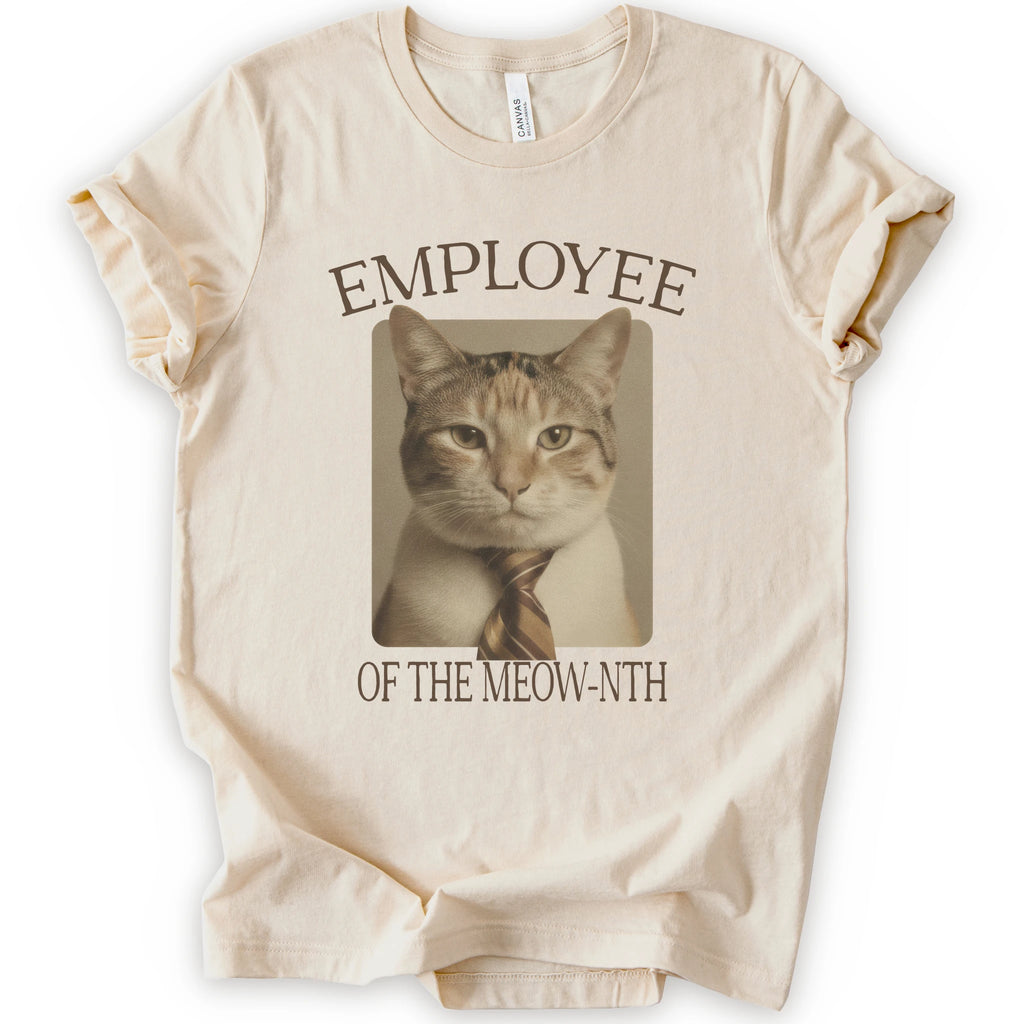A natural short-sleeve crewneck t-shirt with a graphic print of a cat wearing a tie inside a beige frame, with the text 'EMPLOYEE OF THE MEOW-NTH' in brown lettering.