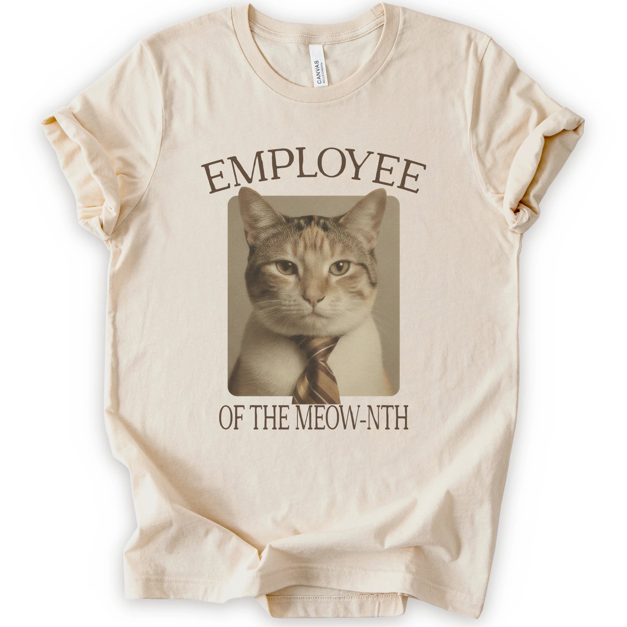 A natural short-sleeve crewneck t-shirt with a graphic print of a cat wearing a tie inside a beige frame, with the text 'EMPLOYEE OF THE MEOW-NTH' in brown lettering.