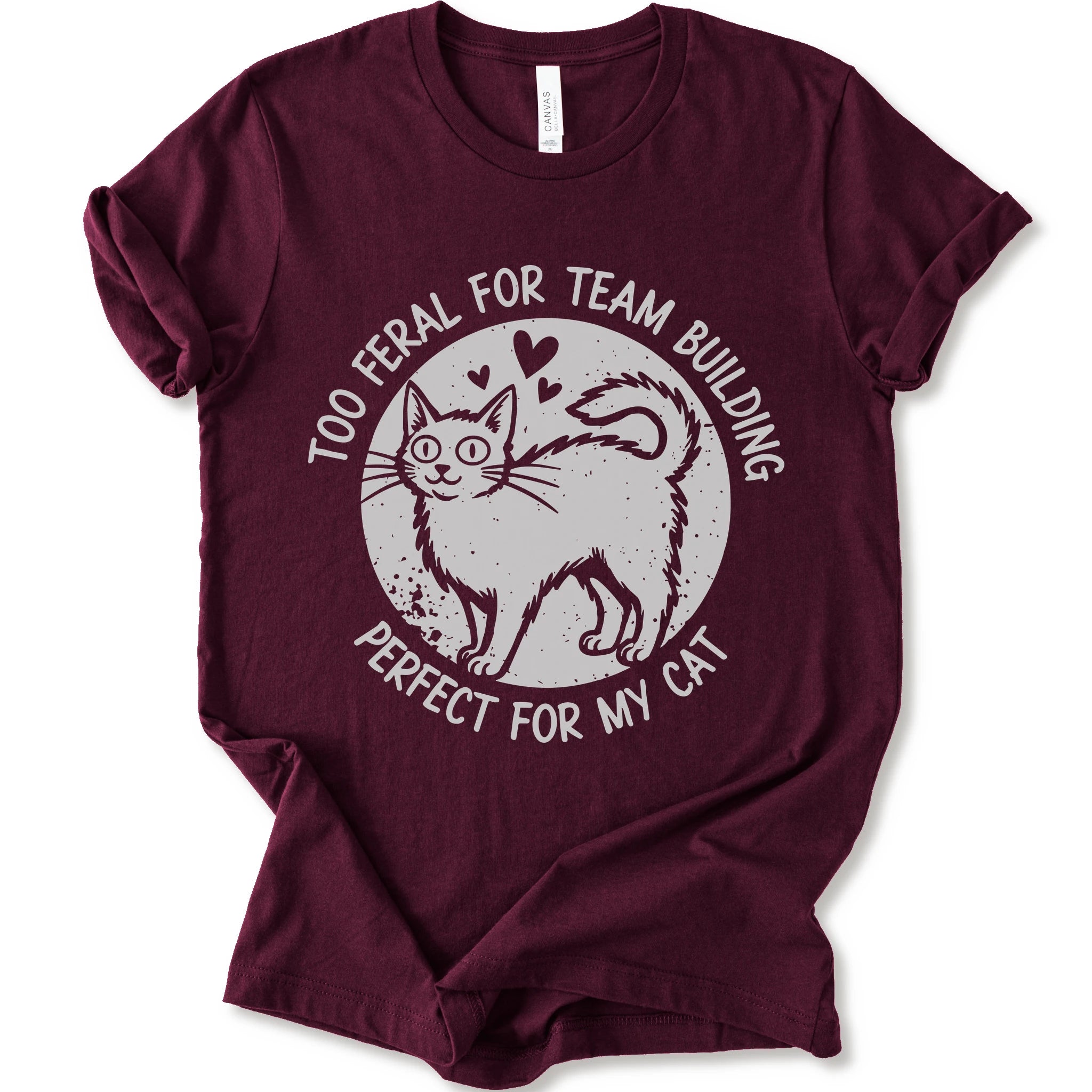 A maroon short-sleeve crewneck t-shirt with a distressed white graphic of a cat inside a circle, surrounded by the text 'TOO FERAL FOR TEAM BUILDING' and 'PERFECT FOR MY CAT'.