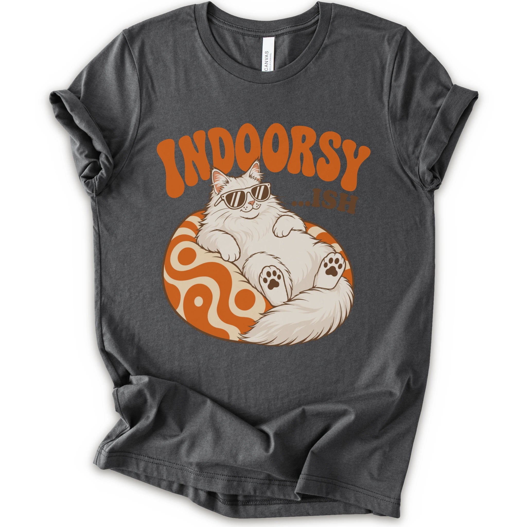 A asphalt short-sleeve crewneck t-shirt with a graphic print of a fluffy white Maine Coon cat wearing sunglasses, lounging on an orange and white swirl-patterned sphere. Above the cat, the text reads 'INDOORSY...ish".