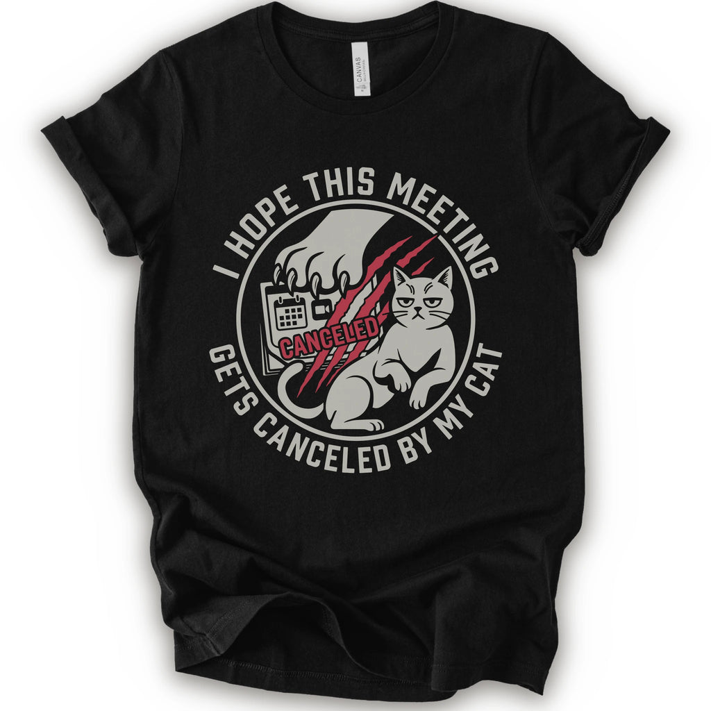 A black short-sleeve crewneck t-shirt with a circular graphic on the front. The graphic features a white cat, a hand scratching, and the text 'I HOPE THIS MEETING GETS CANCELLED BY MY CAT' in white, with 'CANCELLED' written in red script.