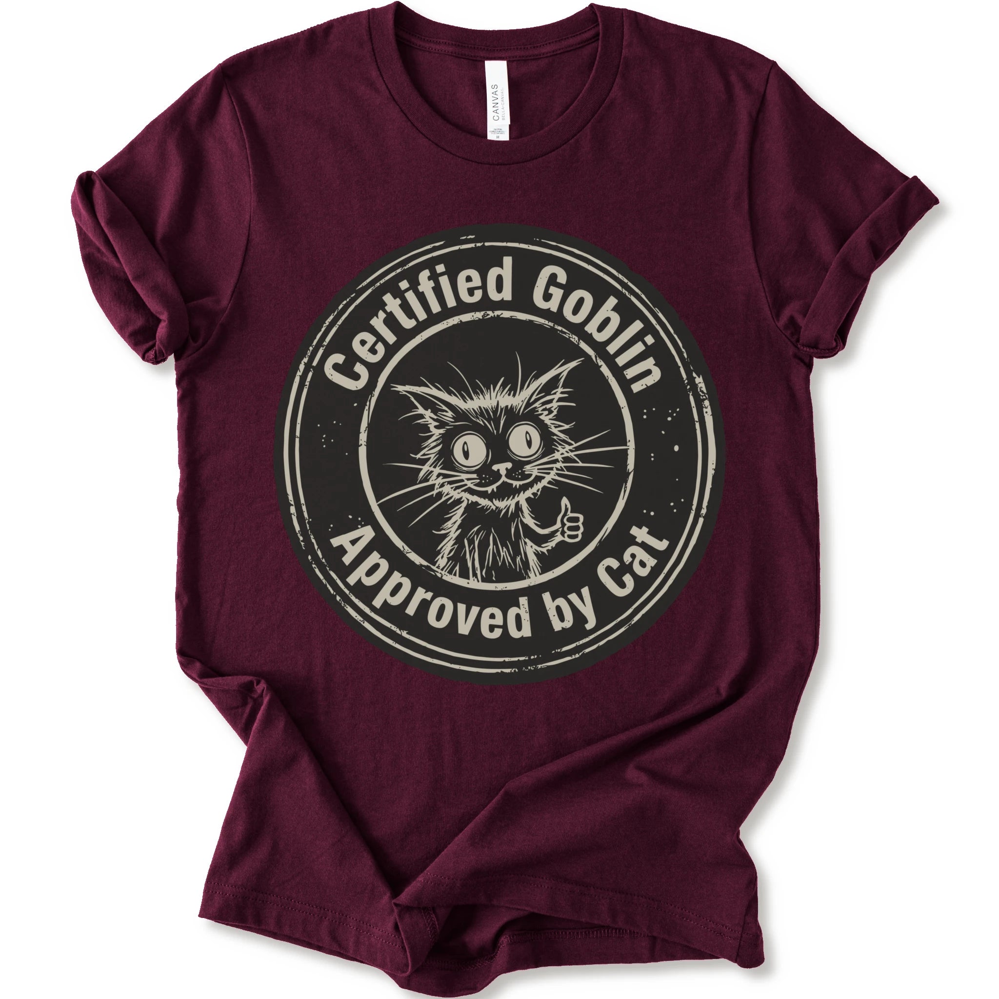 A maroon crewneck t-shirt with a distressed beige-black circular graphic that reads 'Certified Goblin Approved by Cat' around an illustration of a cat giving a thumbs-up.