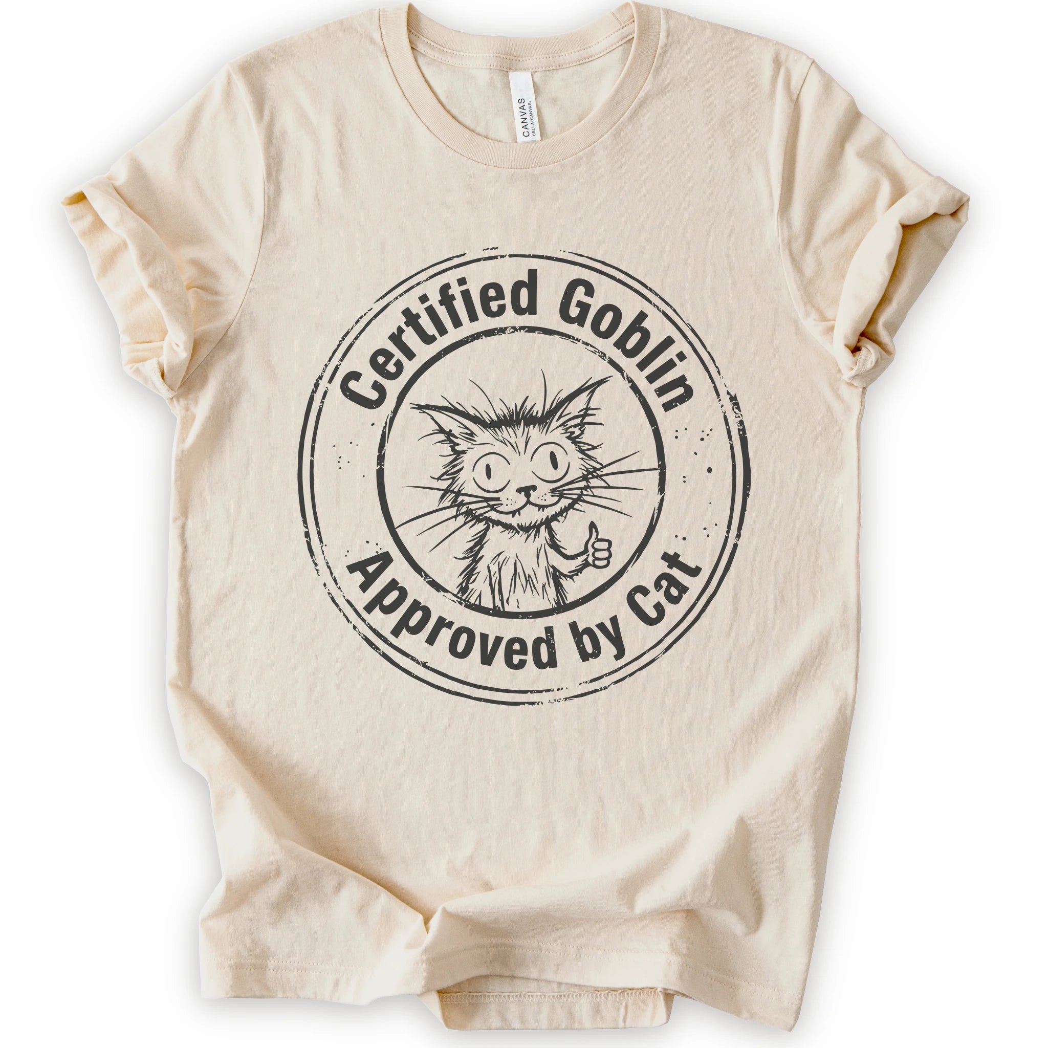 A natural crewneck t-shirt with a distressed black circular graphic that reads 'Certified Goblin Approved by Cat' around an illustration of a cat giving a thumbs-up.