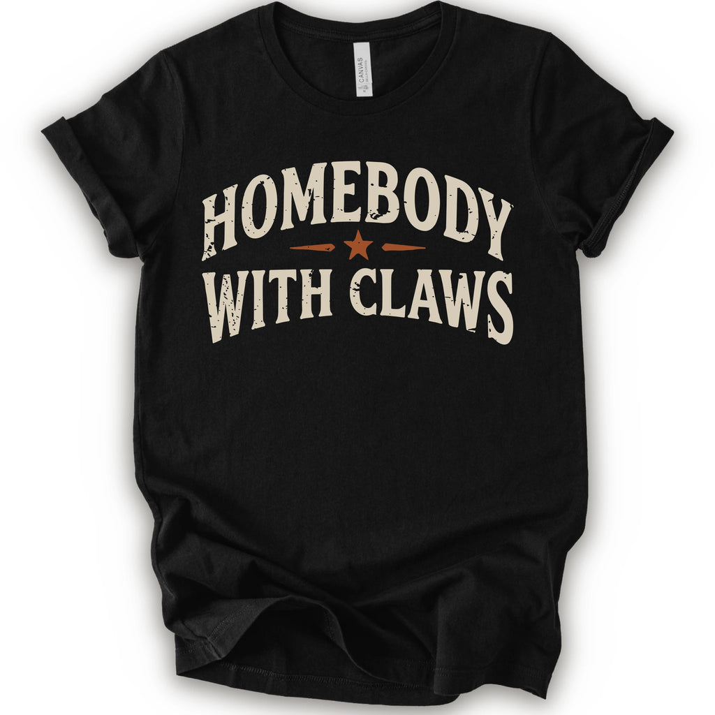 A black short-sleeve t-shirt with a distressed graphic reading 'HOMEBODY WITH CLAWS' in cream lettering and a small orange star accent
