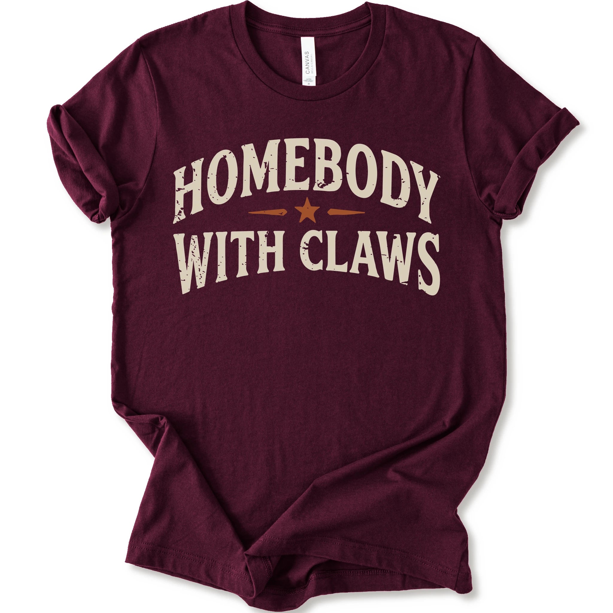 A maroon short-sleeve t-shirt with a distressed graphic reading 'HOMEBODY WITH CLAWS' in cream lettering and a small orange star accent