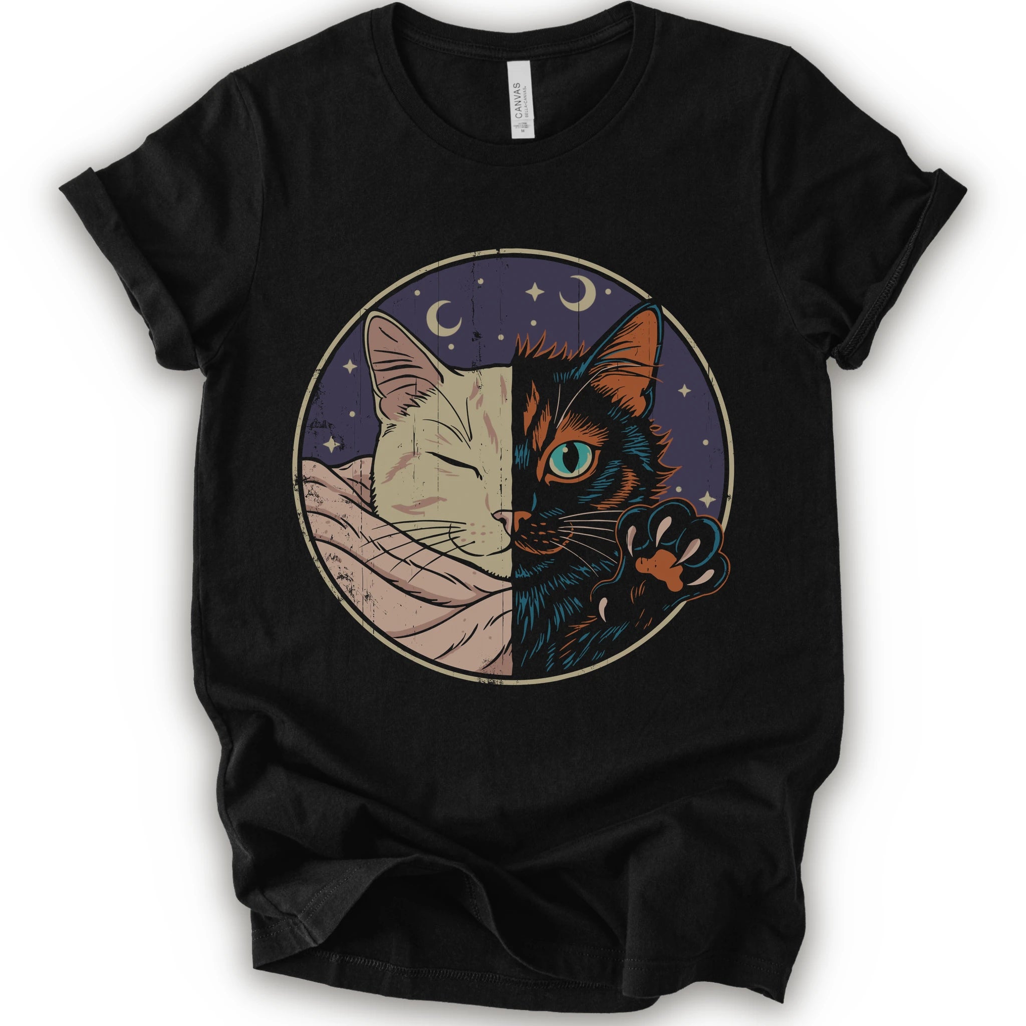 A black short-sleeve crewneck t-shirt featuring a circular graphic print of a split cat design, showing one half as a sleeping cream-colored cat wrapped in a blanket and the other half as a dark black cat with a glowing blue eye and paw resting on its head.