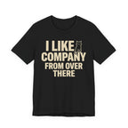 A black short-sleeve t-shirt with a beige graphic print that reads "I Like Company From Over There" with an unimpressed sitting cat