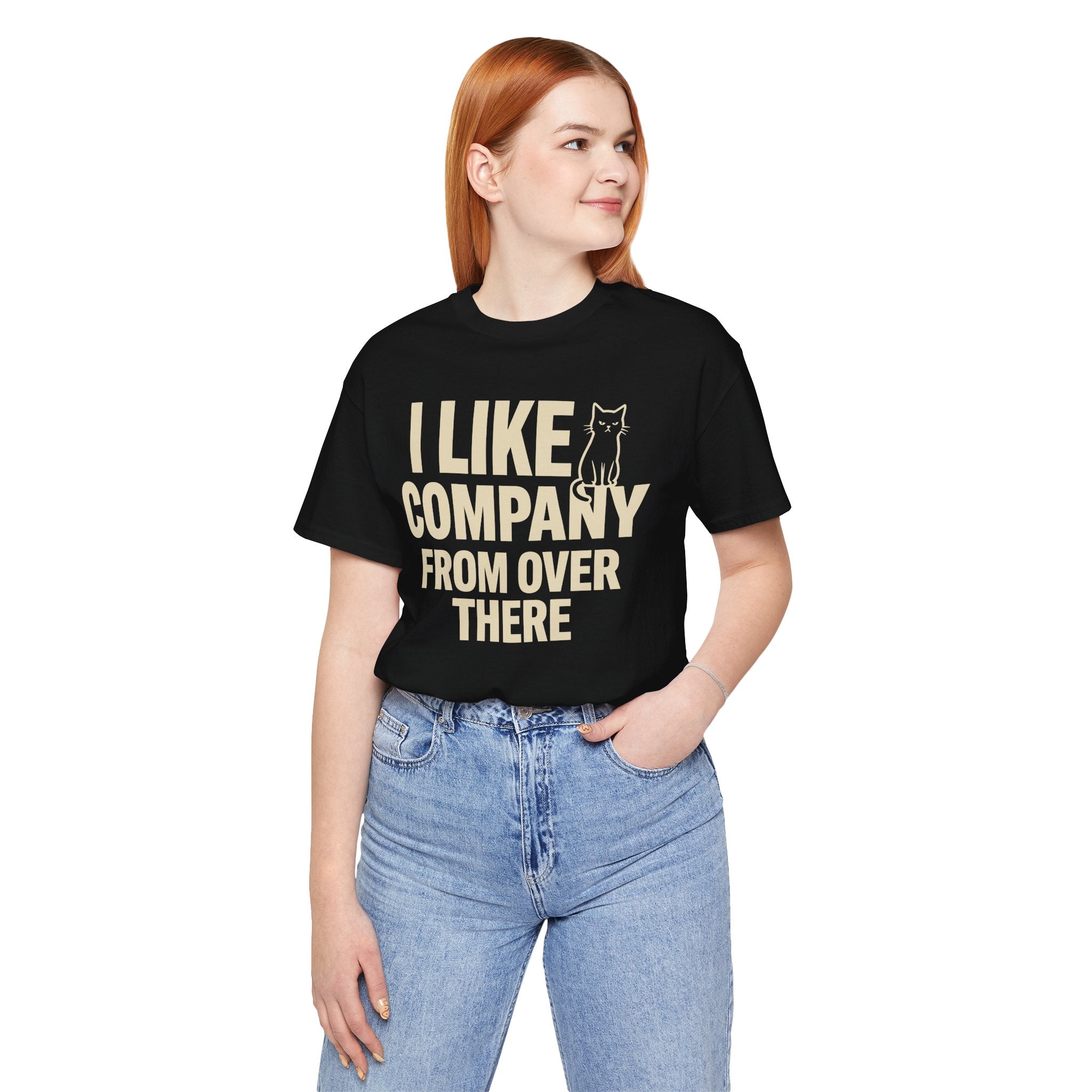 A woman wearing a black short-sleeve graphic t-shirt with cream text that reads 'I LIKE COMPANY FROM OVER THERE' next to a small cat silhouette, paired with light blue jeans, against a plain white background.
