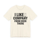 A natural short-sleeve t-shirt with a black graphic print that reads "I Like Company From Over There" with an unimpressed sitting cat