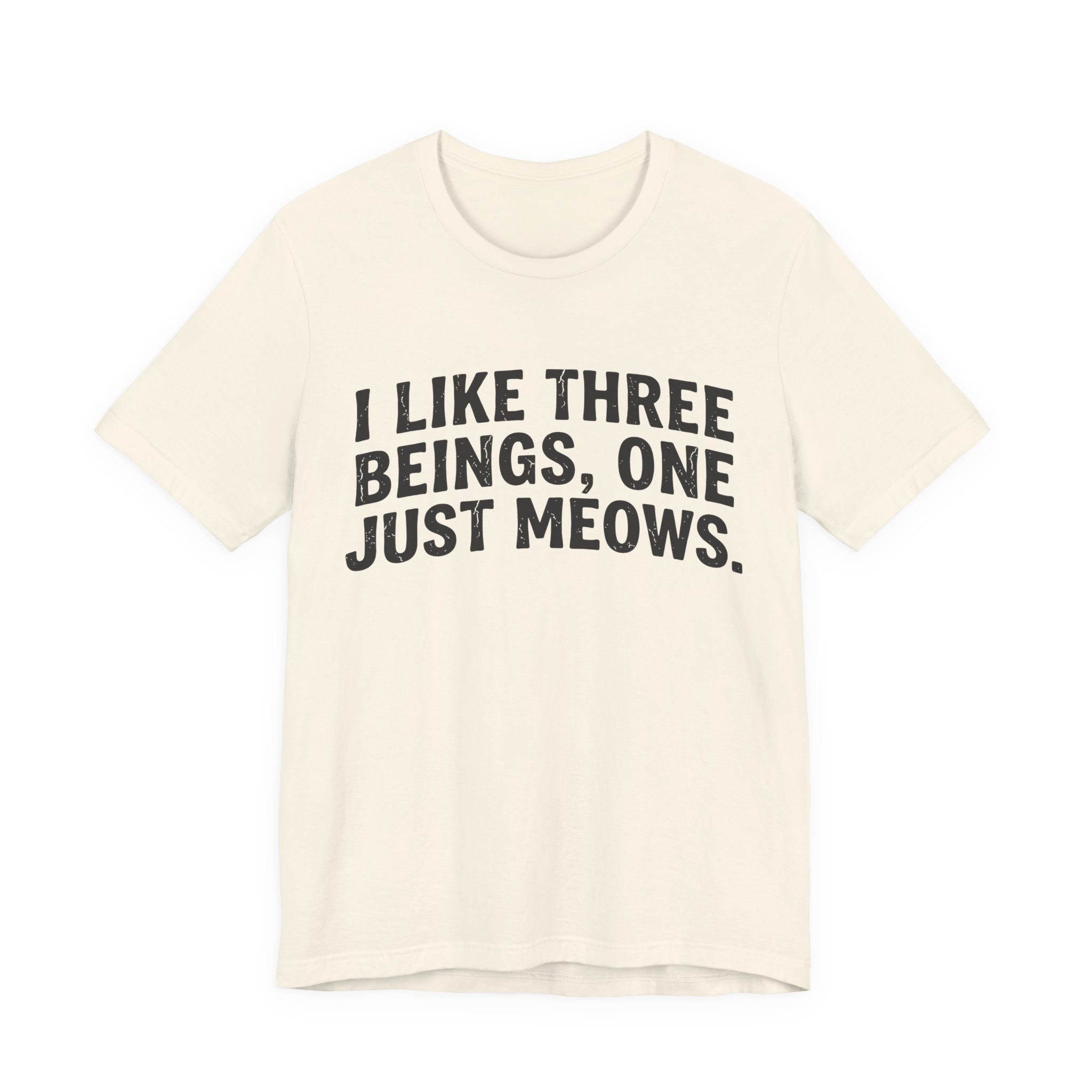 A natural short-sleeve crewneck t-shirt featuring a graphic with Distressed black text reading “I LIKE THREE BEINGS, ONE JUST MEOWS.” 