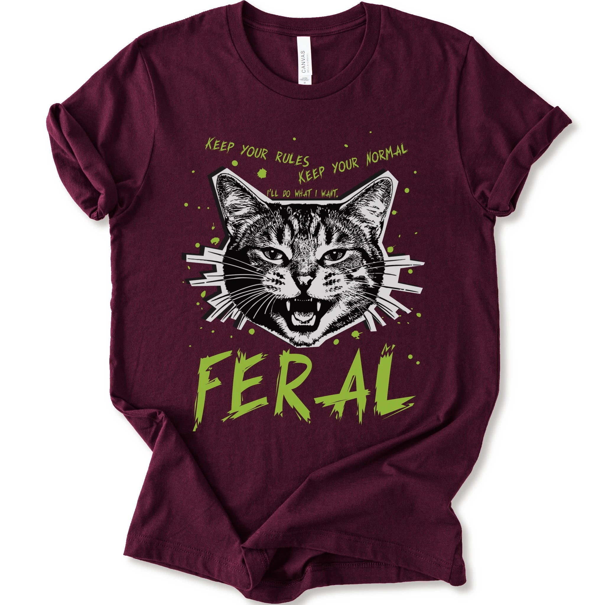 A maroon short-sleeve graphic t-shirt featuring a stylized illustration of a cat's face with the text 'KEEP YOUR RULES KEEP YOUR NORMAL' above and 'FERAL' in distressed lime green below.