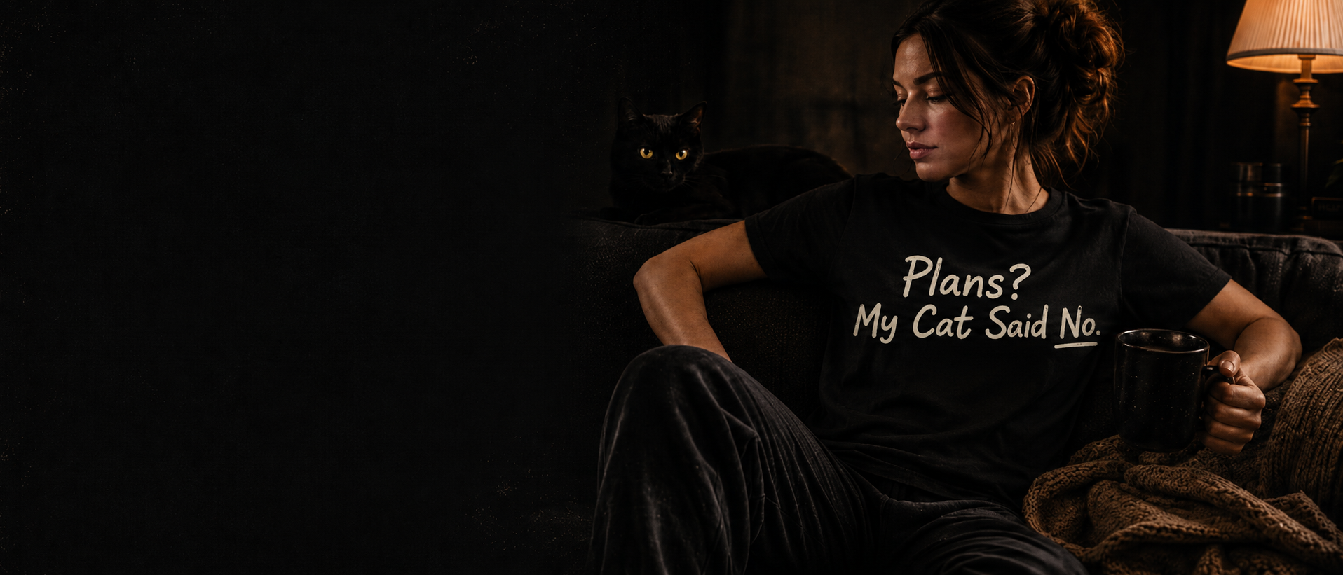 Woman wearing a black “Plans? My Cat Said No.” T-shirt beside a black cat.