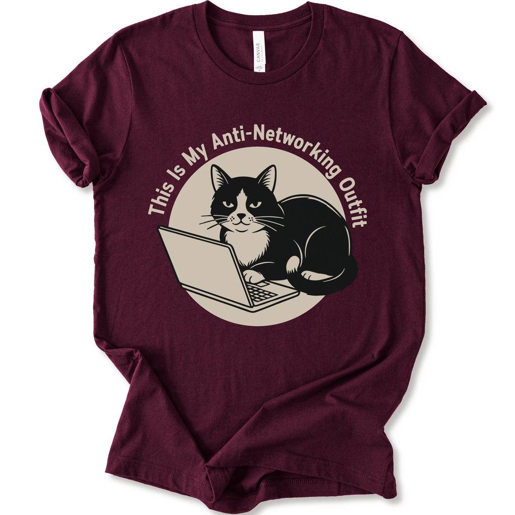 A maroon T-shirt with a “This Is My Anti-Networking Outfit” curves above a black-and-white cat sitting at an open laptop. The artwork uses a clean circular badge layout with a limited black-and-cream palette.